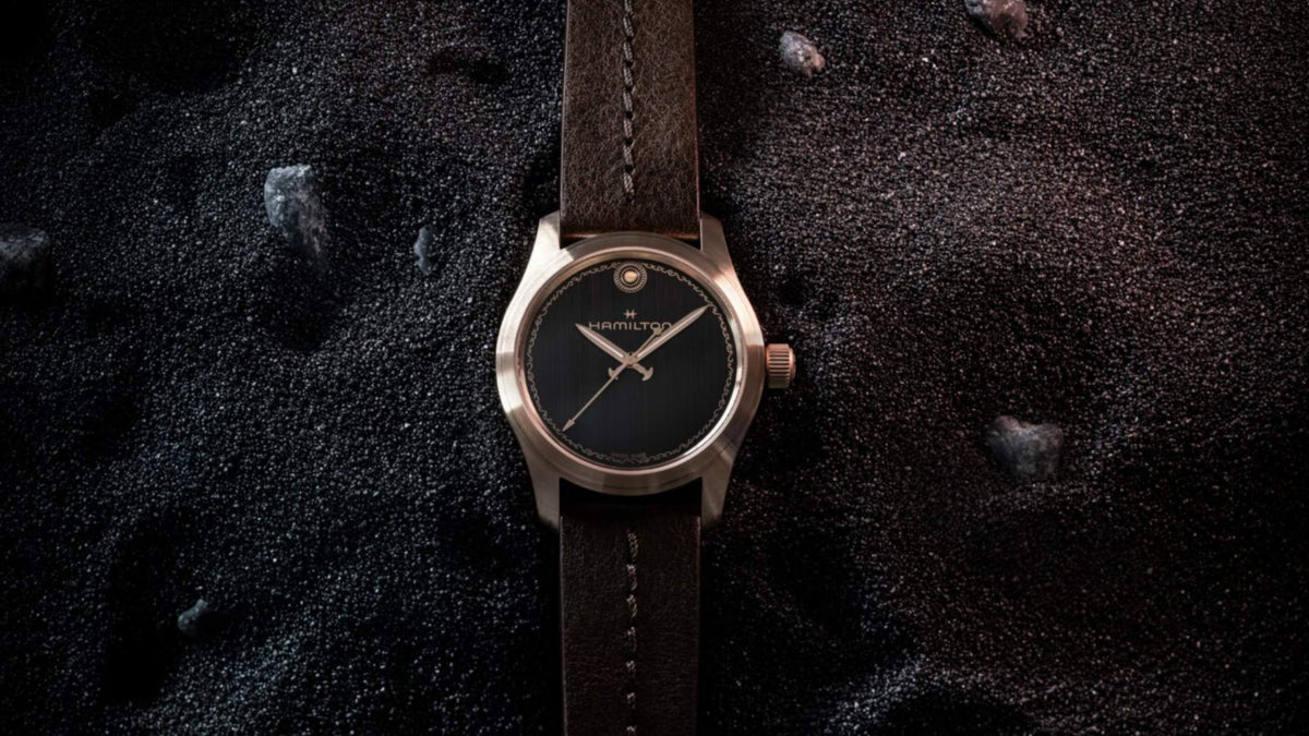 Hamilton Khaki Field Auto The Odyssey watch with a black dial and brown leather strap resting on black volcanic sand