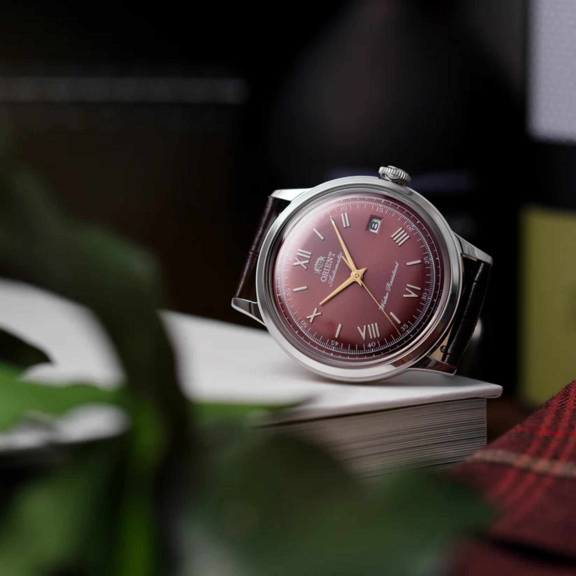 Orient Bambino RA-AC0026R30B bordeaux dial automatic watch displayed on stack of books in lifestyle setting