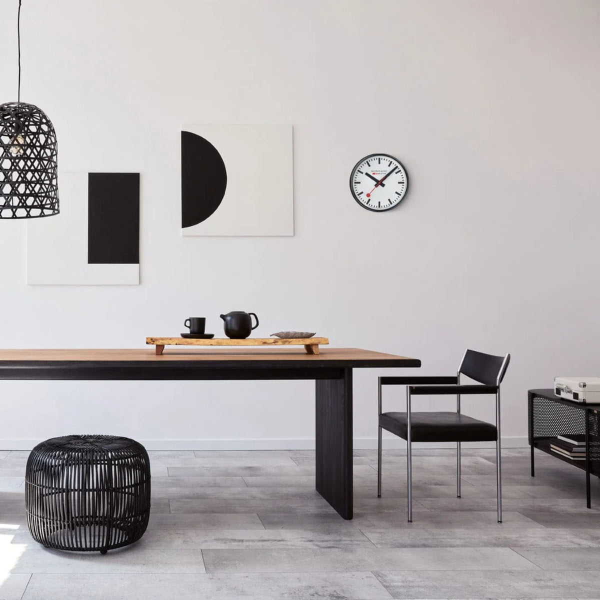 Mondaine black wall clock A990.CLOCK.12SBB displayed on a modern dining room wall with Scandinavian minimalist decor