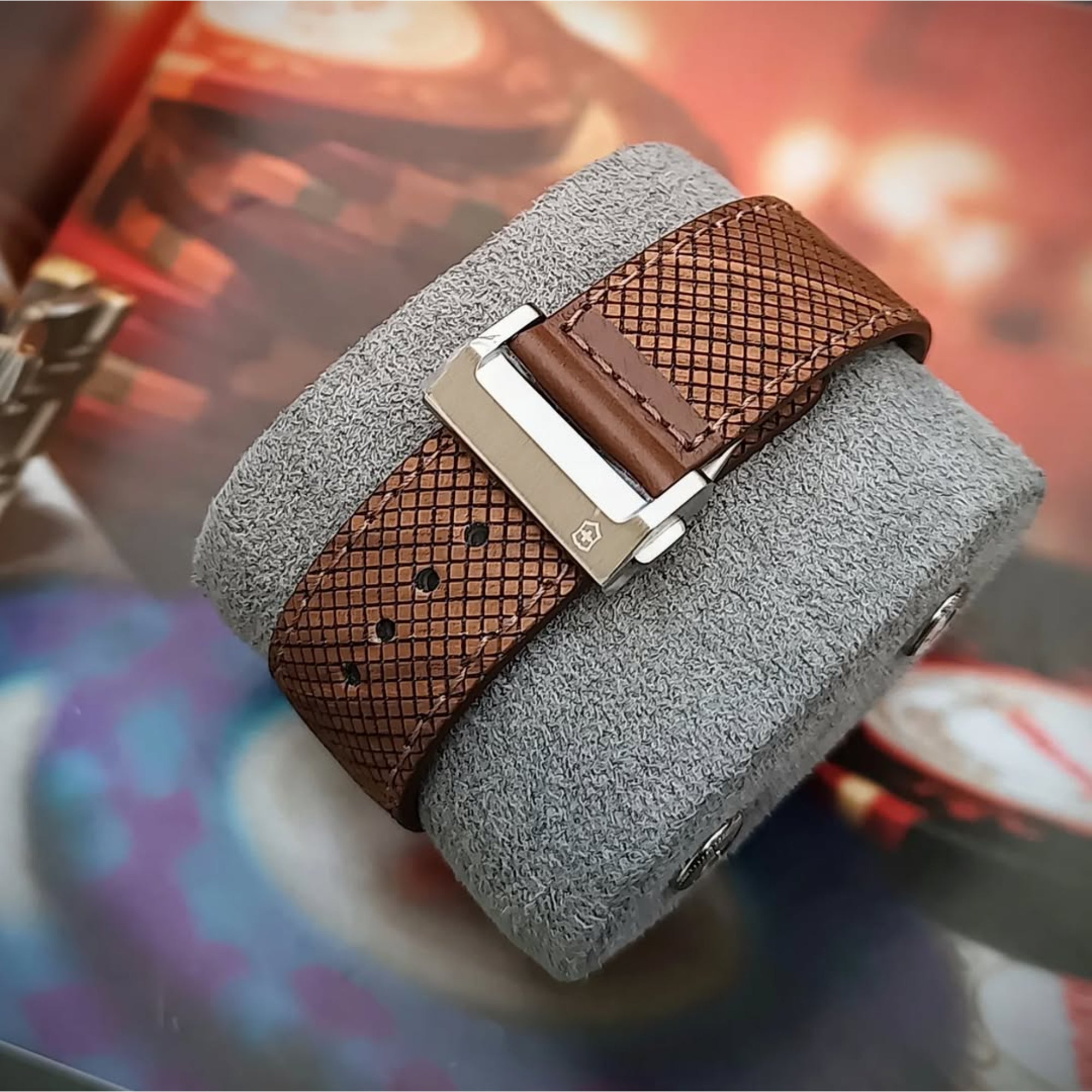 A close-up of a textured brown cross-hatch watch strap fastened around a gray display cushion with a stainless steel deployment clasp