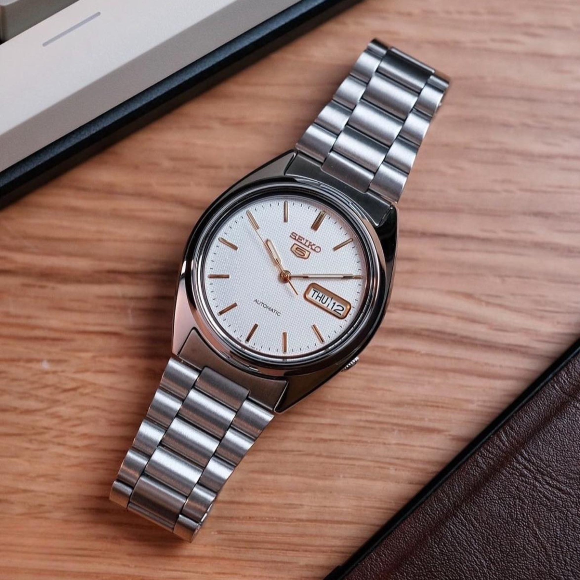 Seiko 5 SNXG47K1 automatic watch placed on wooden table with notebook