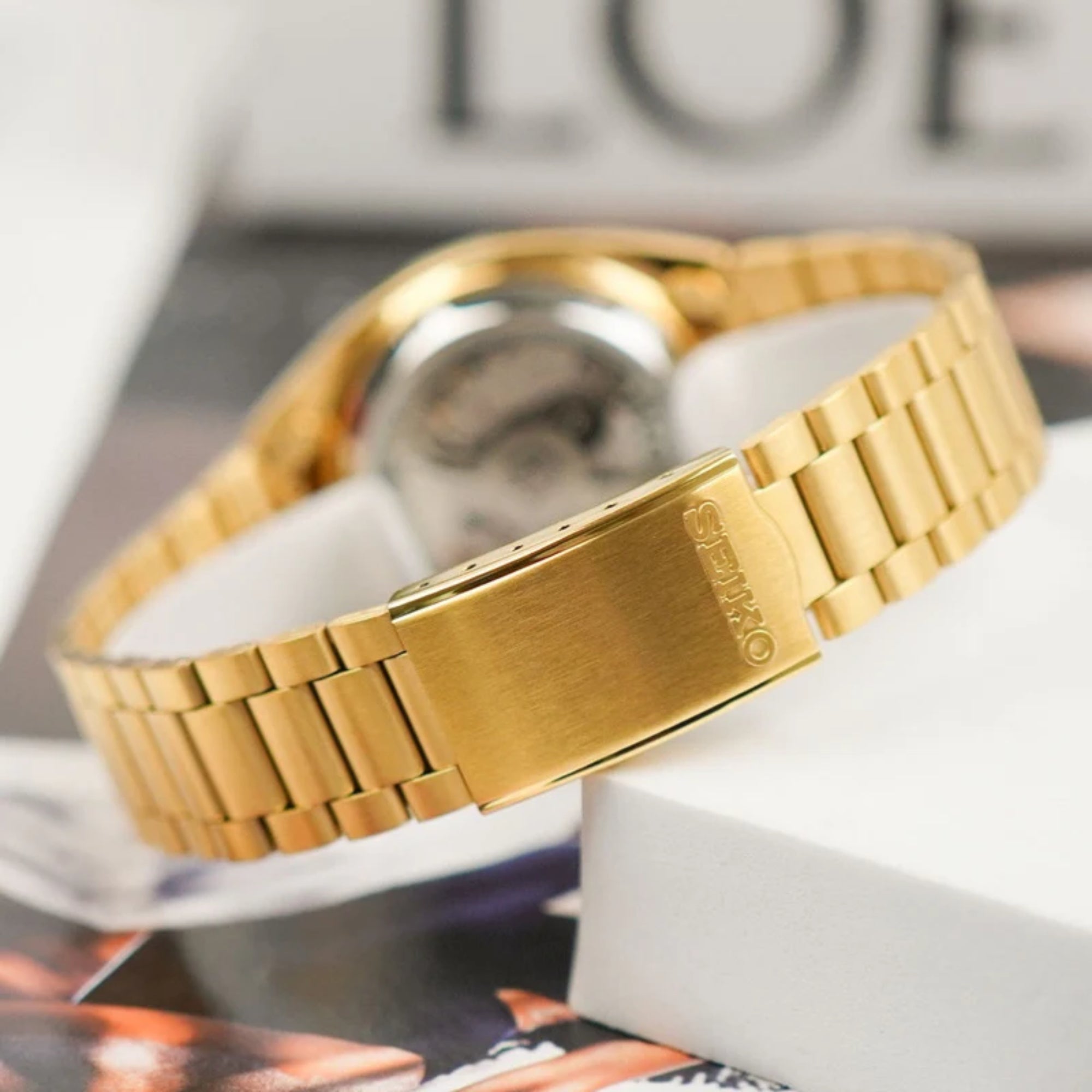Seiko 5 automatic gold dial and yellow gold-tone stainless-steel bracelet with blurred background