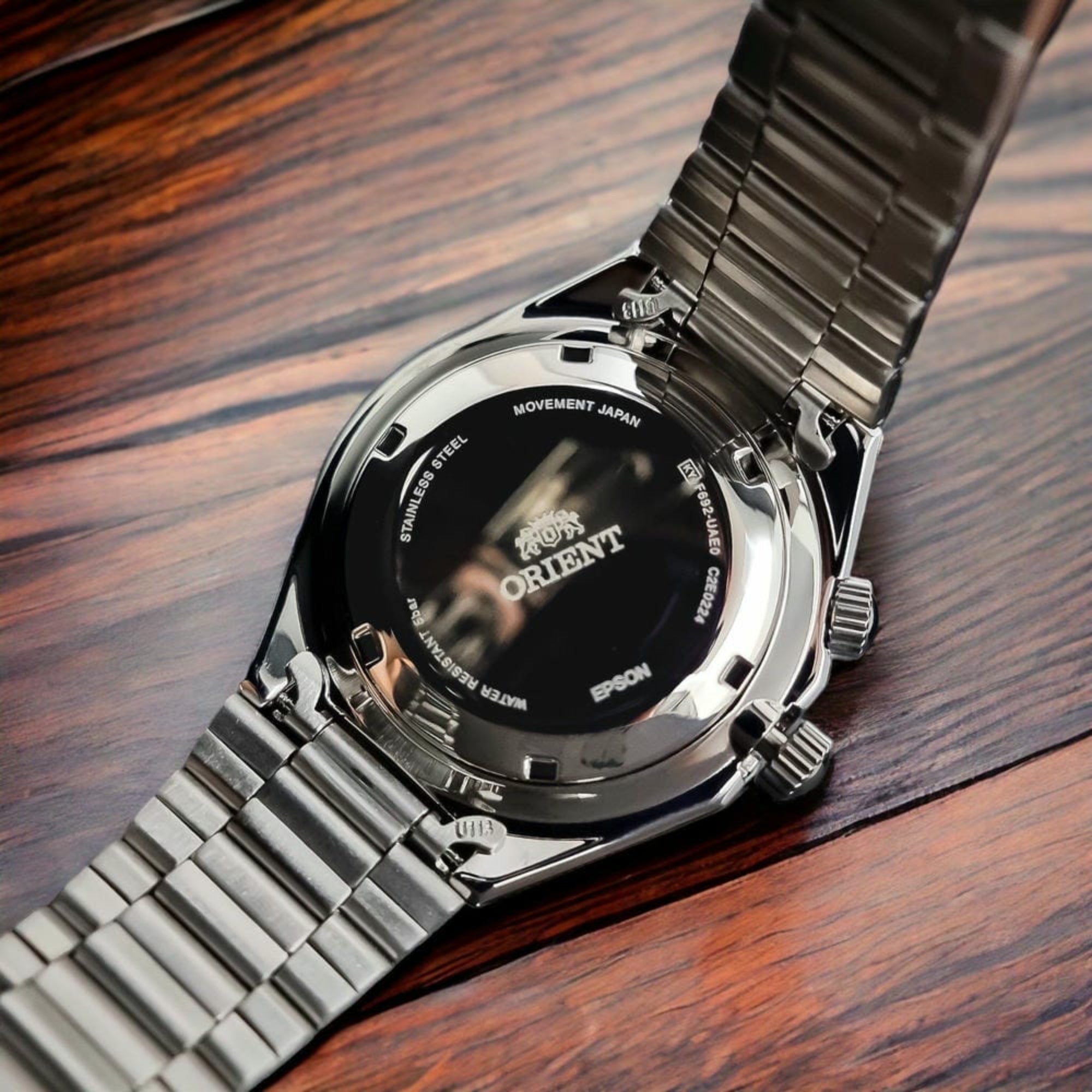 stainless steel screw-down caseback of an Orient Neo 70s watch resting on a wooden surface