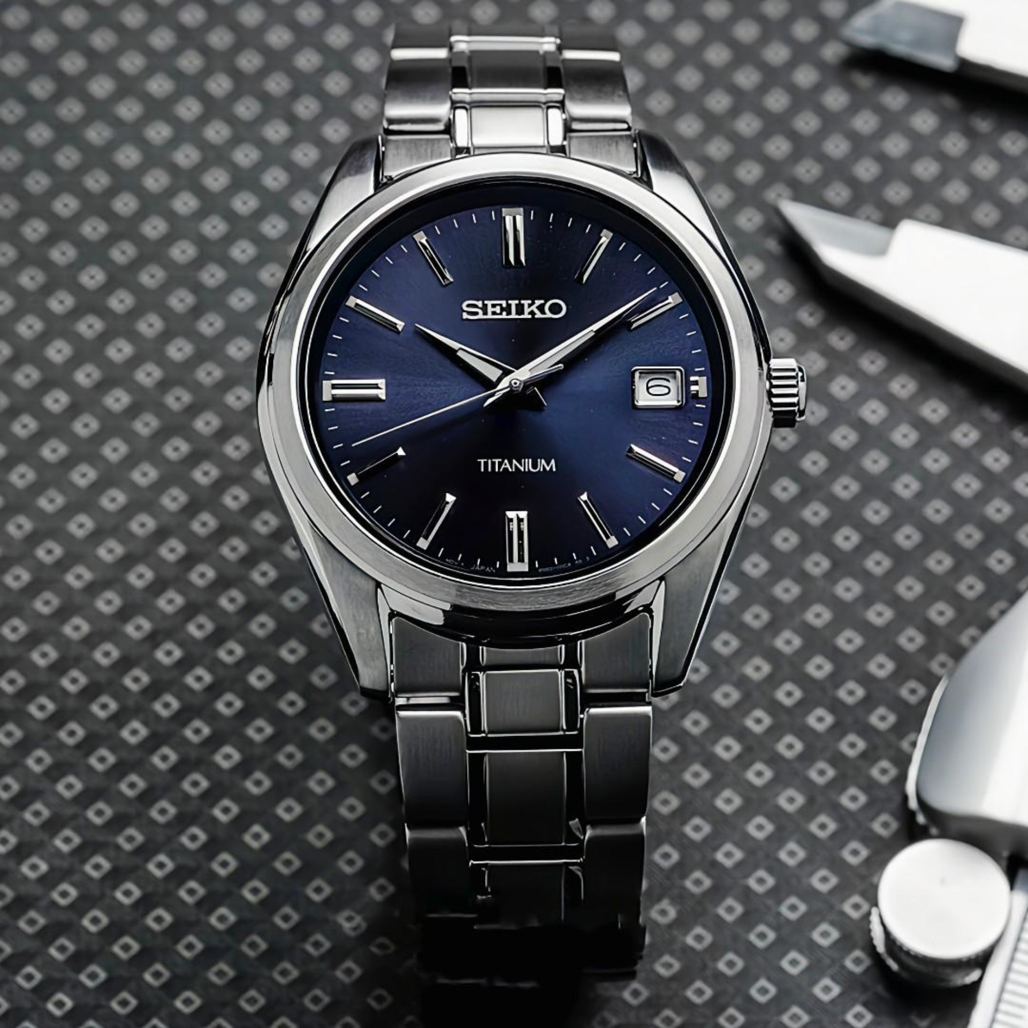 Seiko Essentials 40mm SUR373P1 blue dial titanium quartz watch displayed on textured surface with tools