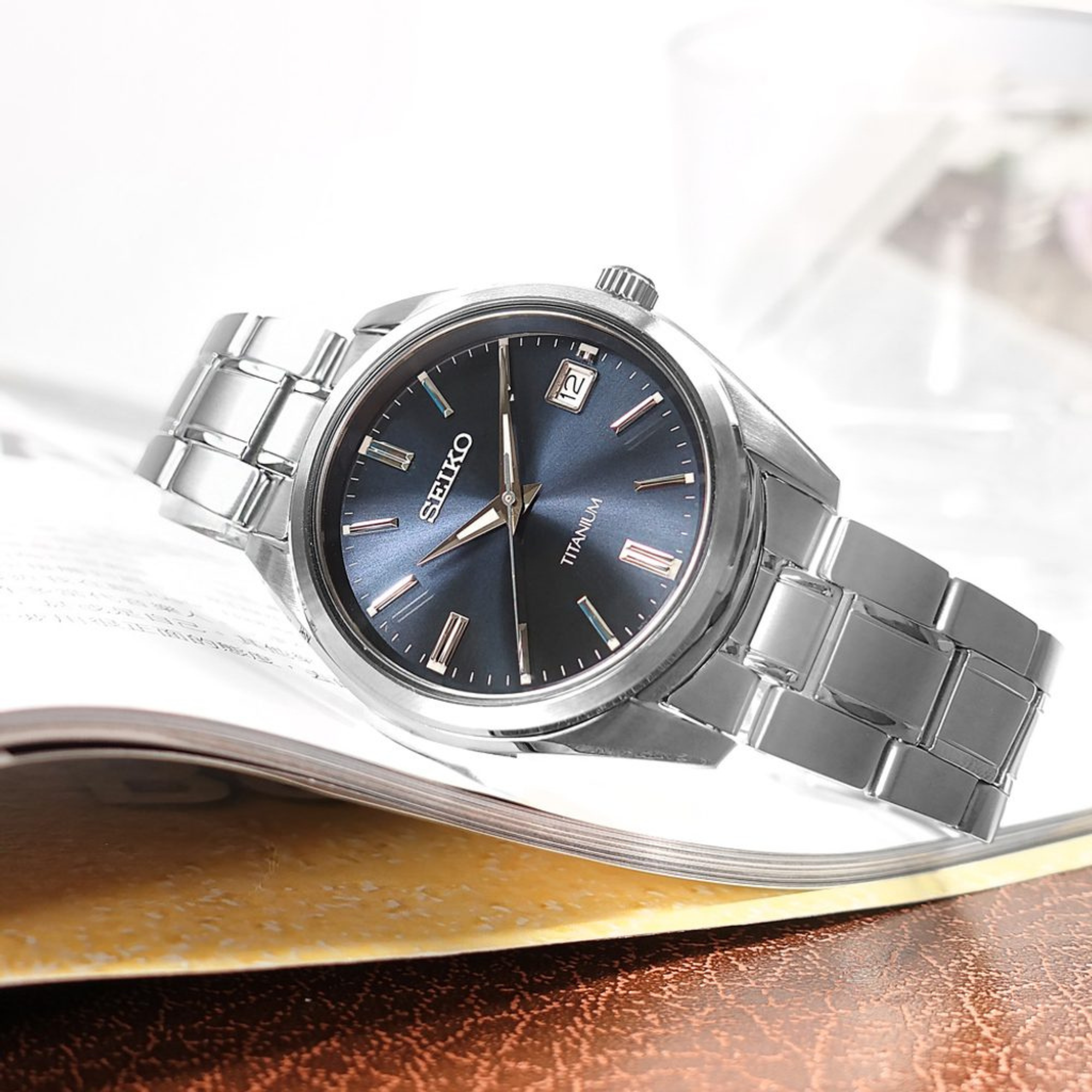 Seiko SUR373P1 titanium watch with blue dial resting on an open book in lifestyle setting