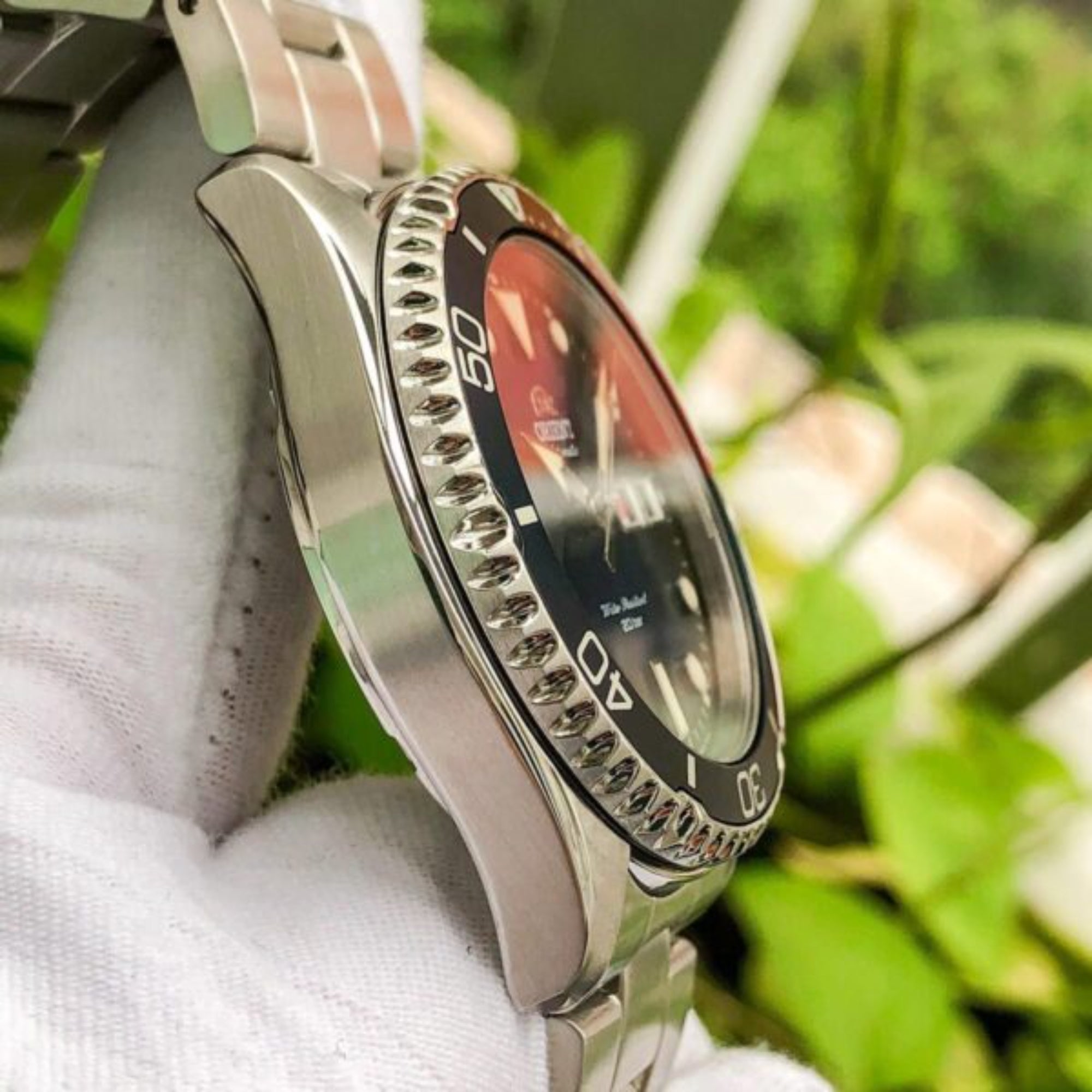 Close-up of a silver wristwatch with a black face held against a blurred green background