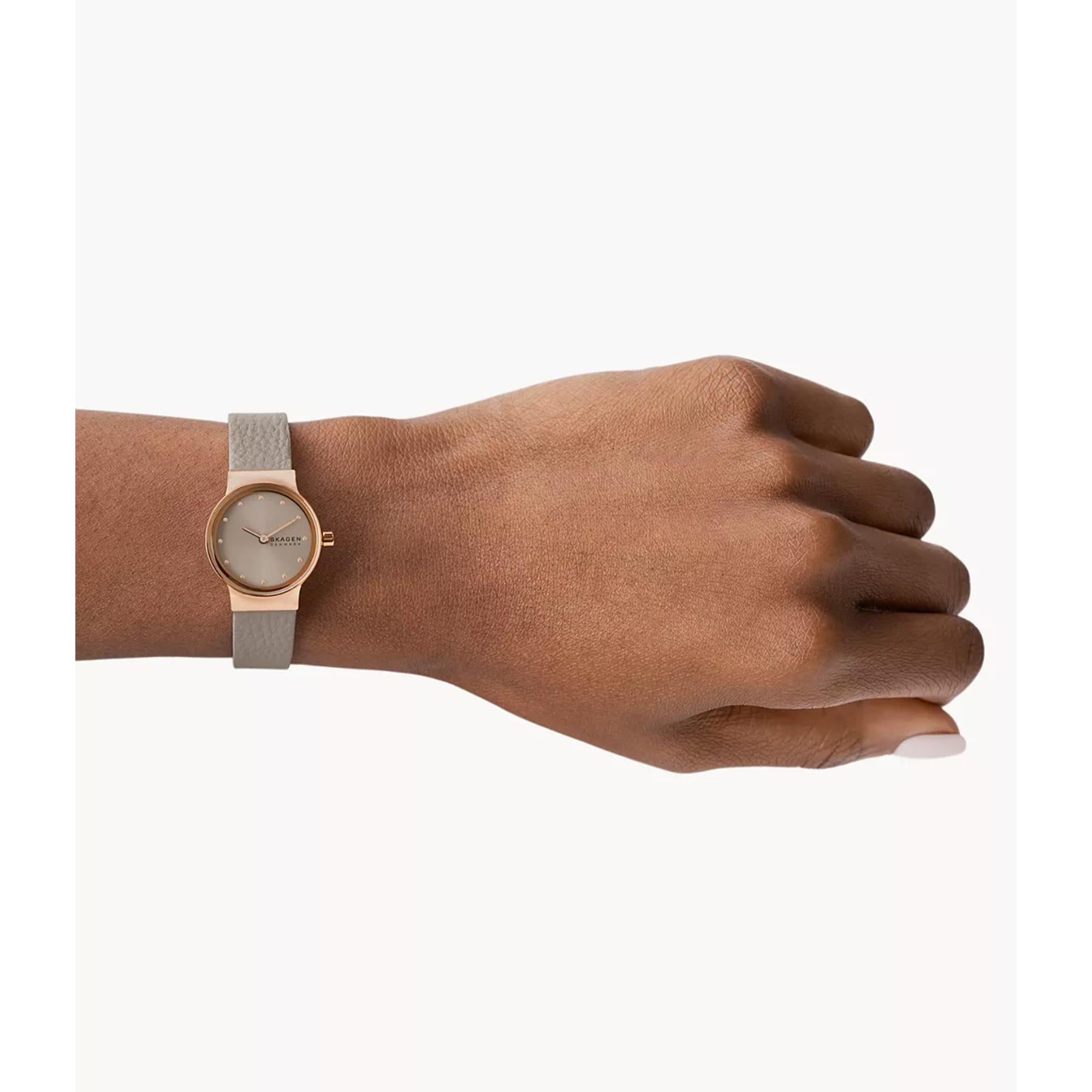 Hand wearing a rose gold watch with a gray strap on a white background