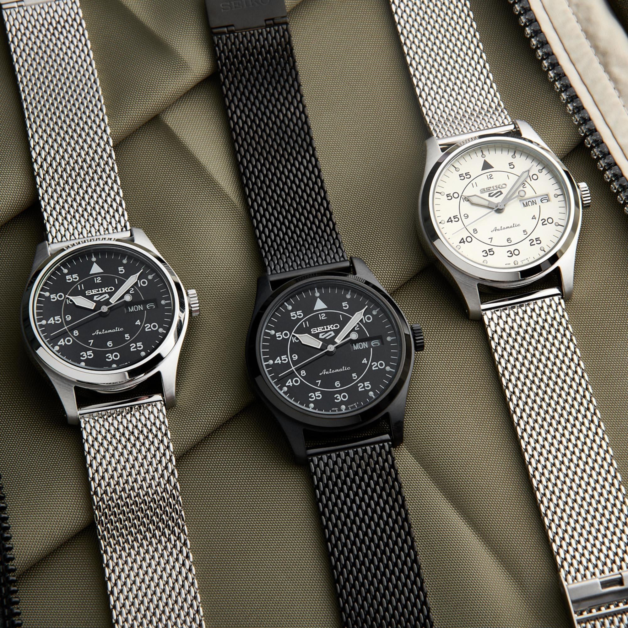 Three Seiko watches with mesh straps on a textured surface