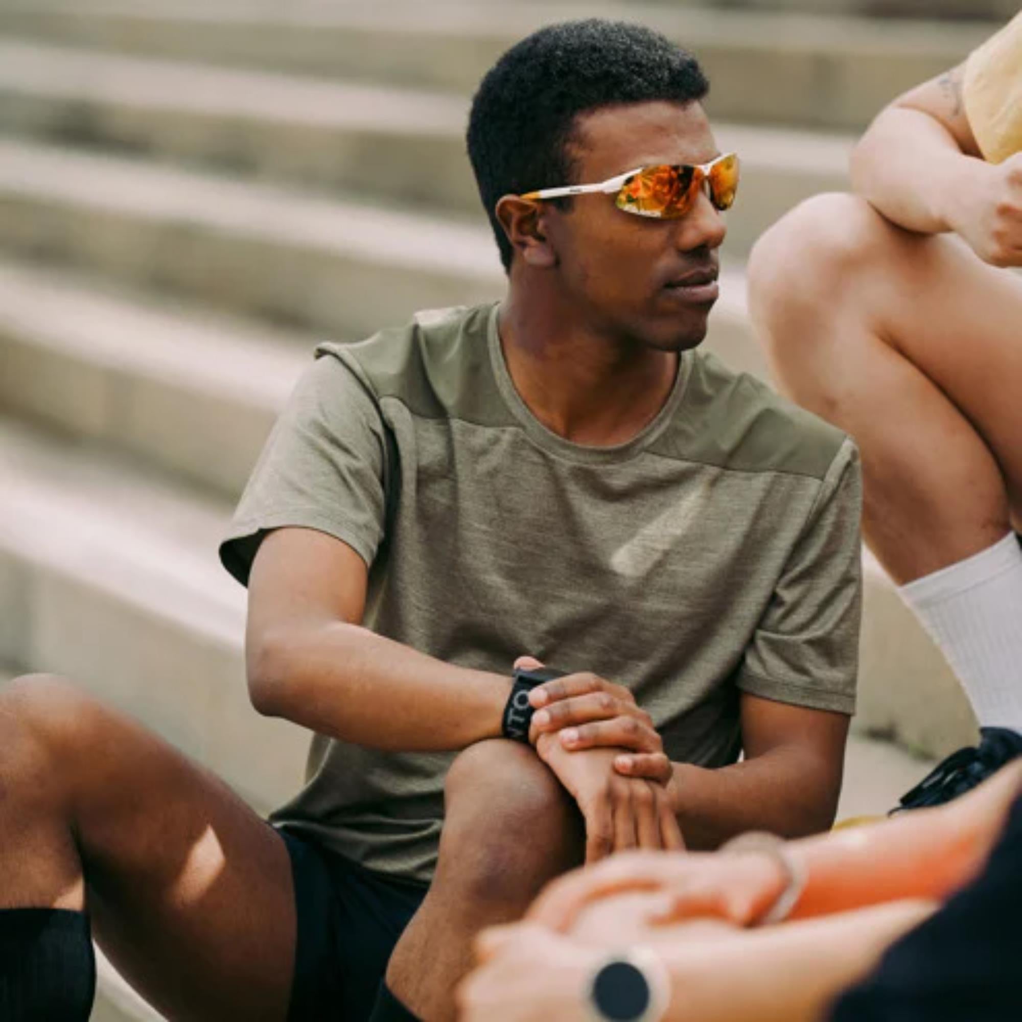 Man wearing sunglasses and a green shirt sitting on steps with another person.
