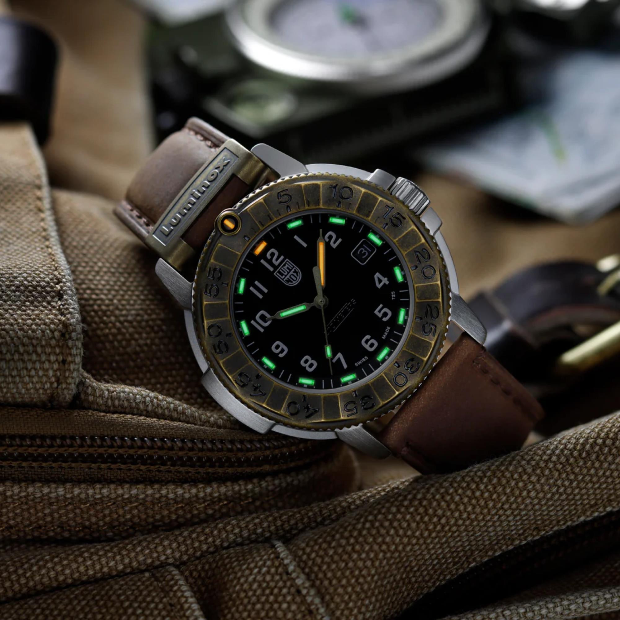 Close-up of Luminox Adventure Watch XL.1301.LG sitting on top of a rugged tan canvas backpack, highlighting the glowing green numerals on its black face and its brown leather strap