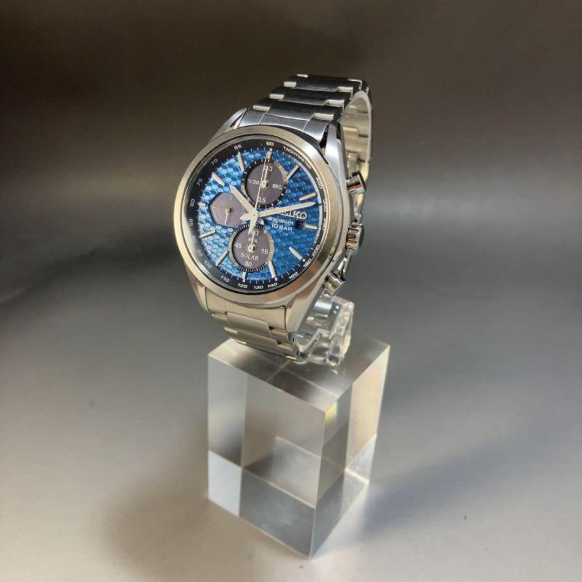Seiko Essentials Solar Chronograph watch SSC801P1 with a blue dial, displayed on a clear acrylic block