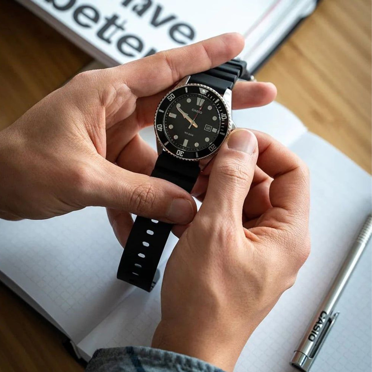 Casio Timeless MDV-107-1A1VEF close-up showing the watch being adjusted over a notebook, highlighting its crown and strap details