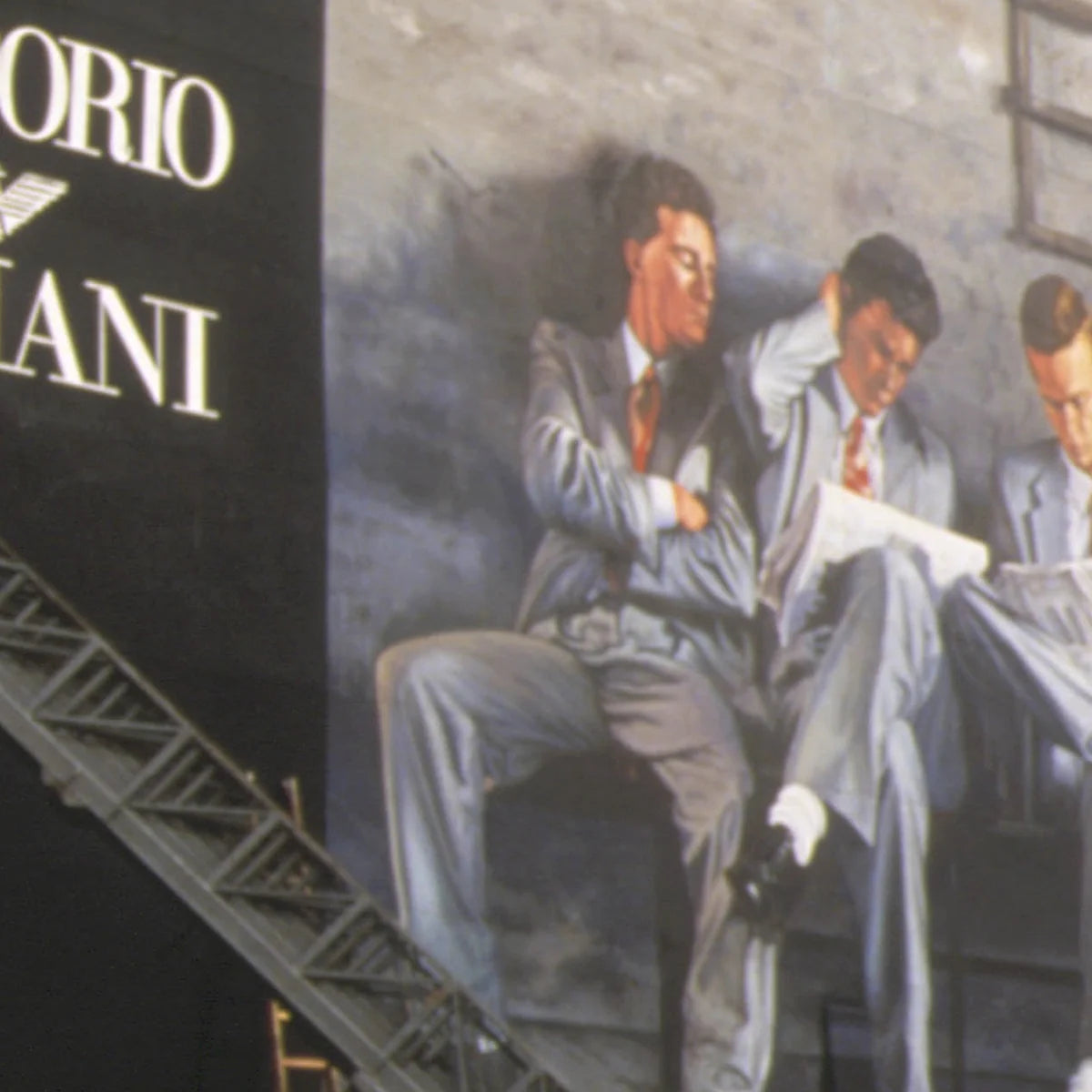 A large painted mural on a building wall showing three men in suits seated and reading, with part of the text 'Emporio Armani' visible on a dark vertical sign beside them