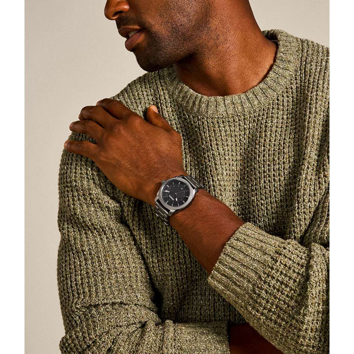 Man wearing a green knitted sweater and a watch with a neutral background