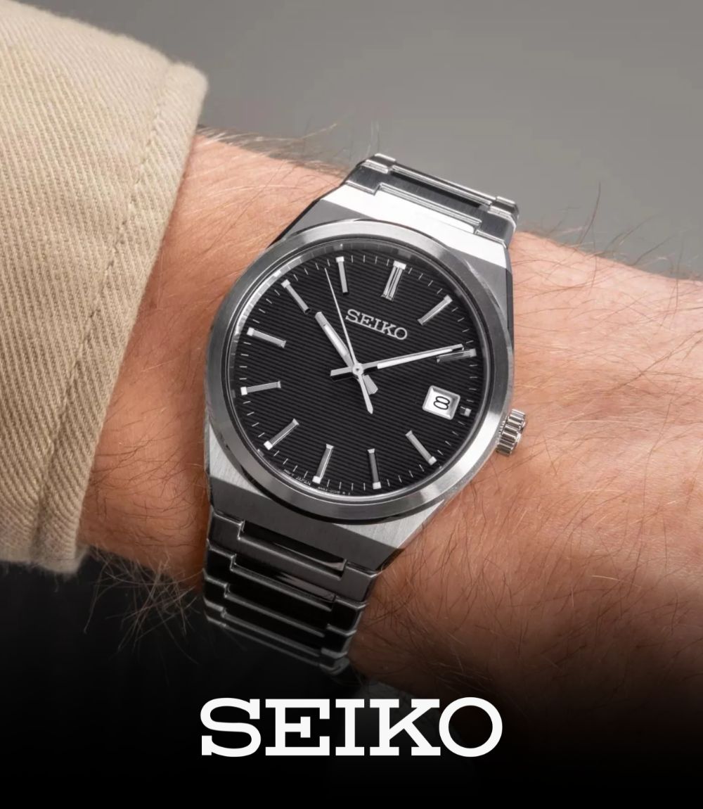Close-up of a Seiko dress watch worn on a wrist, featuring an integrated stainless steel bracelet, a black textured horizontal-pattern dial, and silver hour markers, featuring the Seiko logo at the bottom