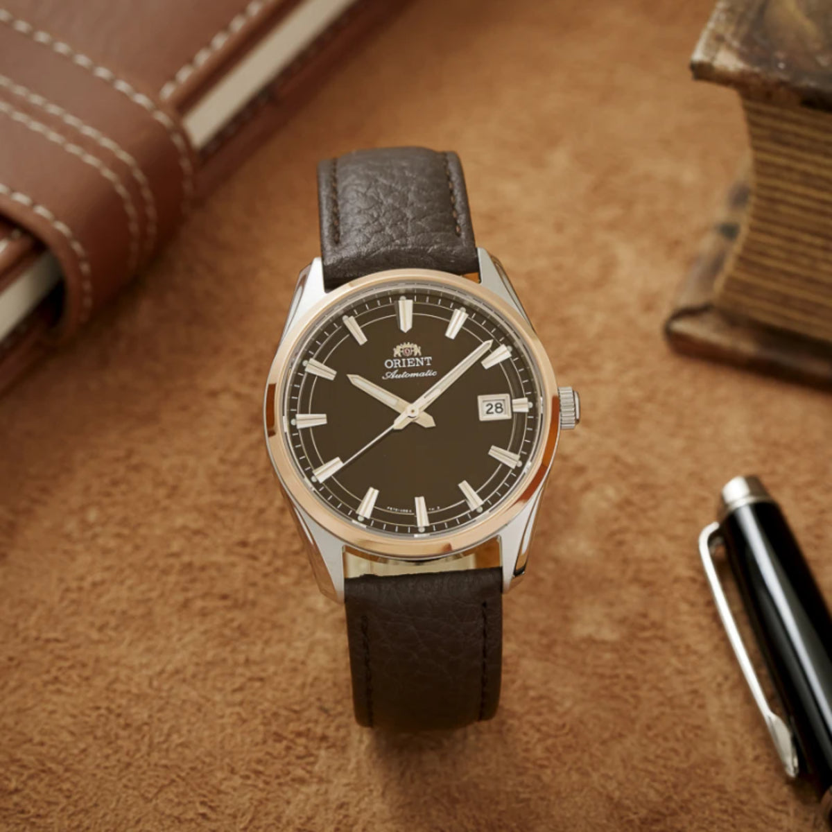 Orient Stretto watch resting flat on a textured brown background