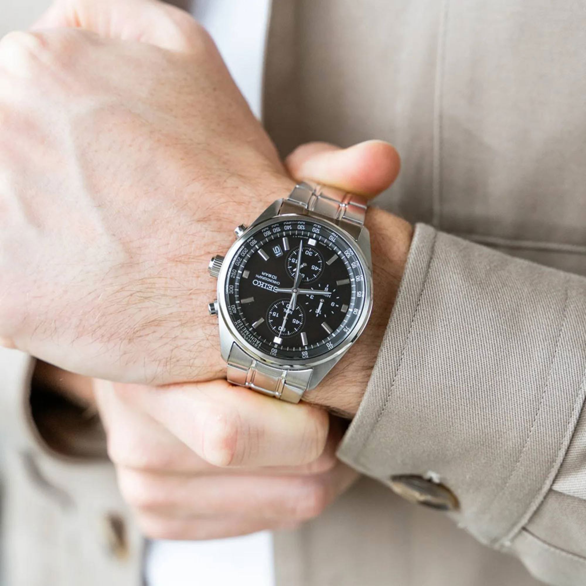 Close-up of a person wearing a silver watch with a black face.