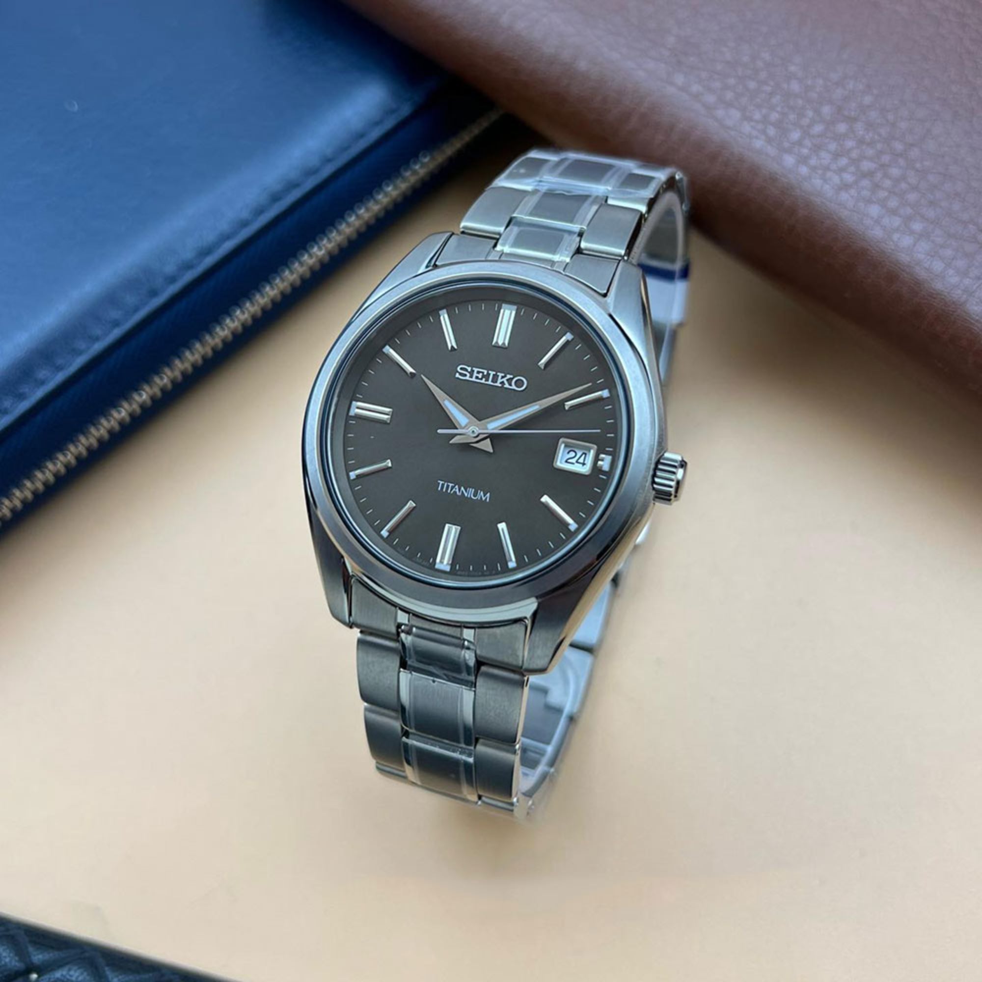 Seiko watch with black dial and titanium bracelet on a beige surface