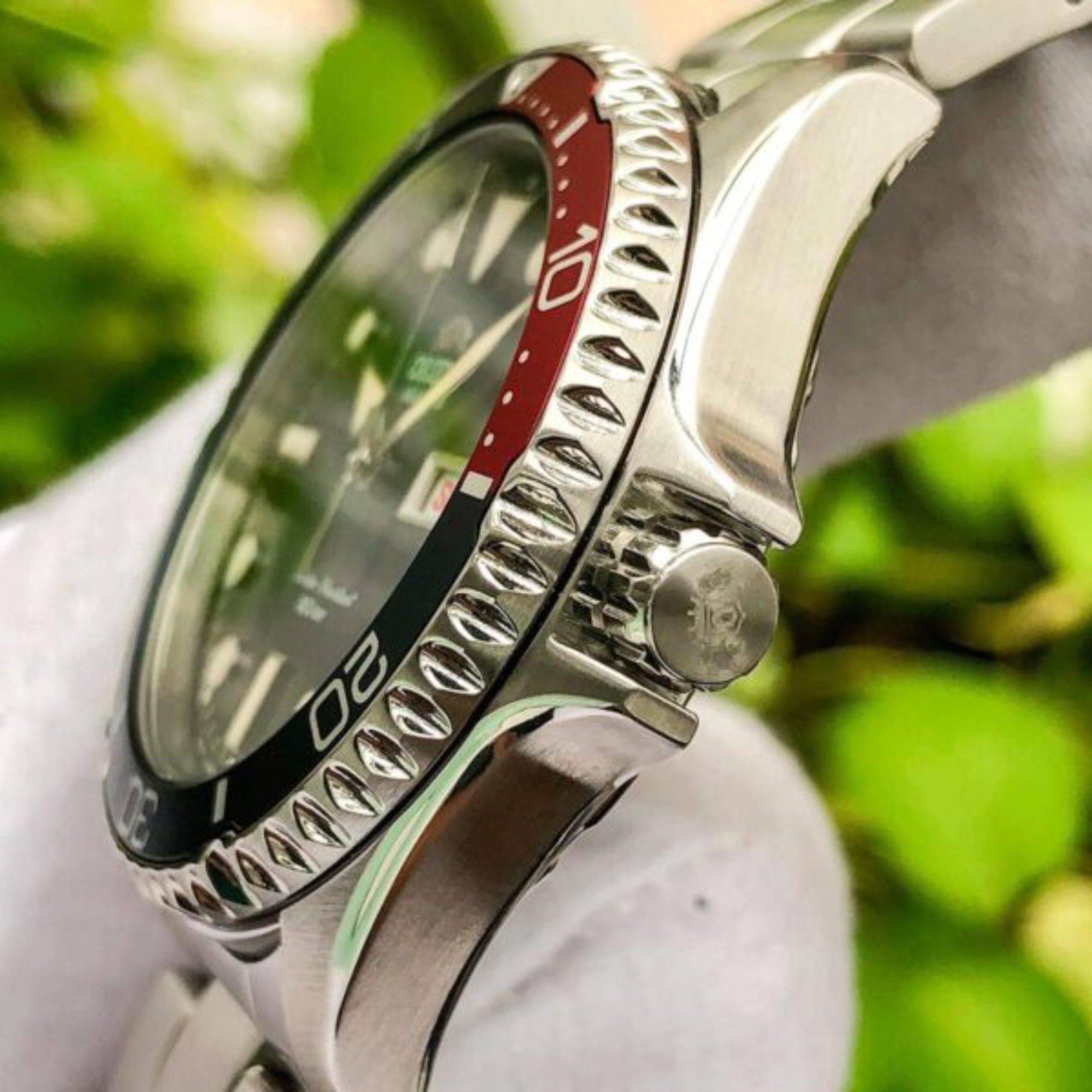 Close-up of a silver watch with a red accent on a blurred green background
