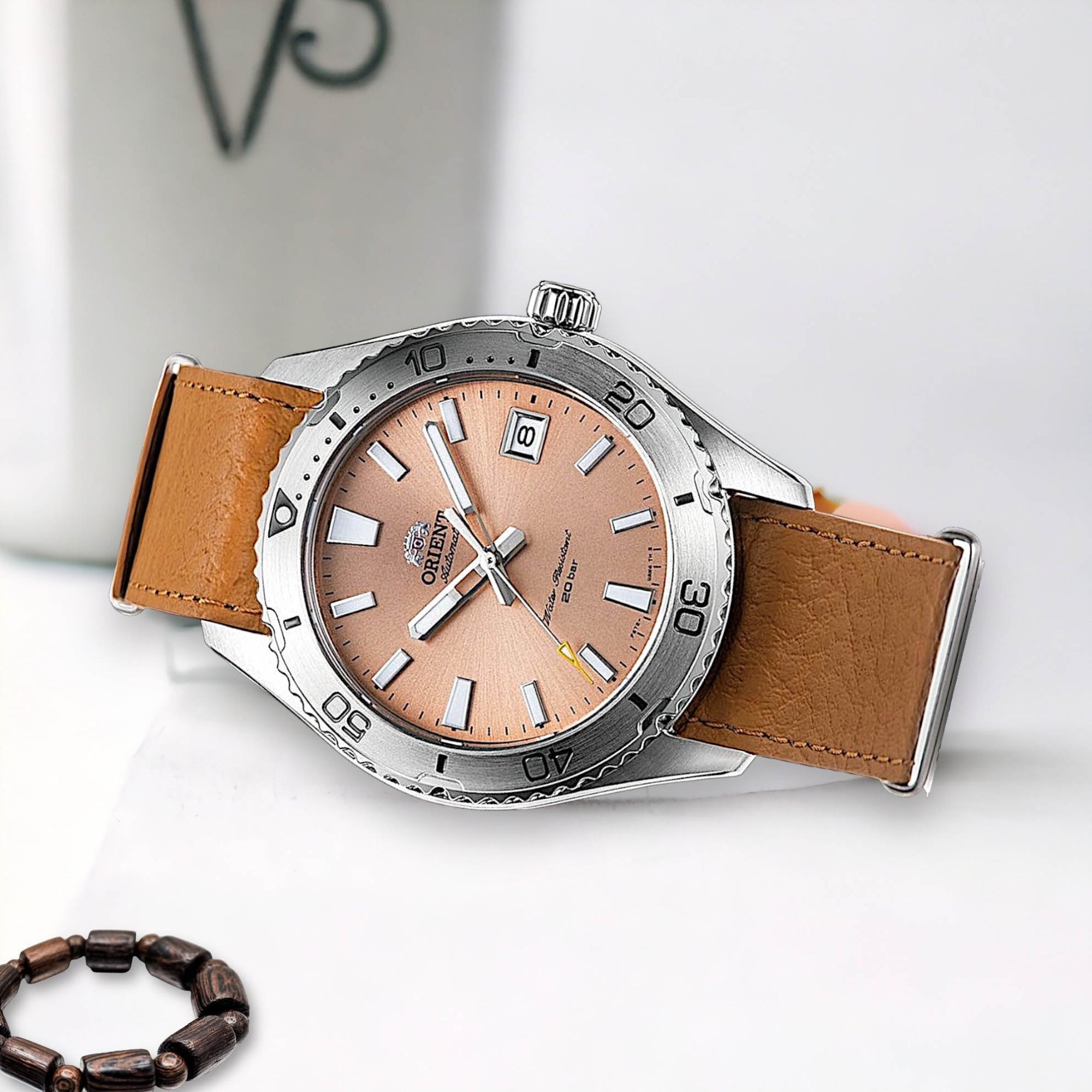 Orient Mako automatic dive watch with a peach sunburst dial and tan leather strap resting on a white surface