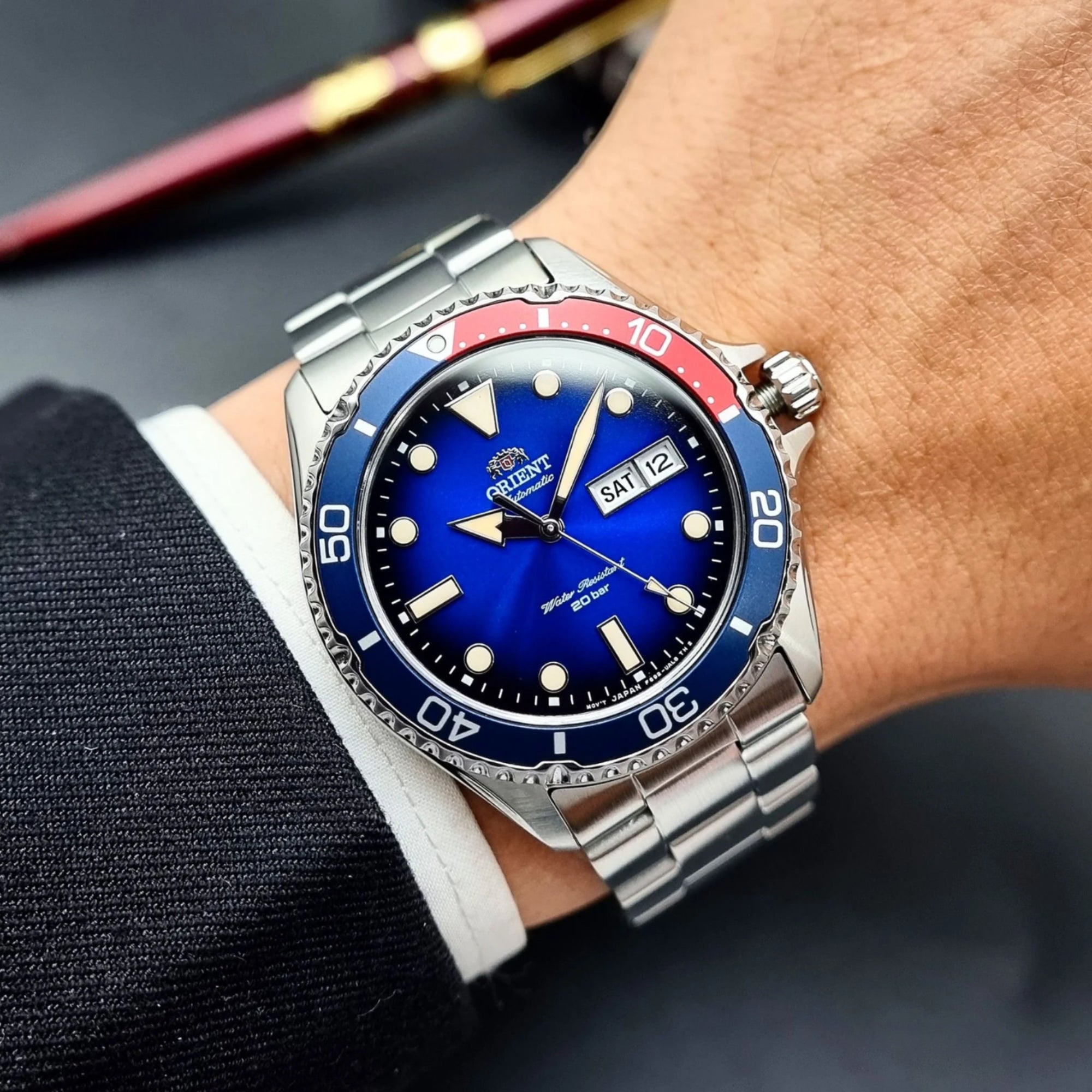 Wrist wearing a silver watch with a blue face and red accents on a dark background