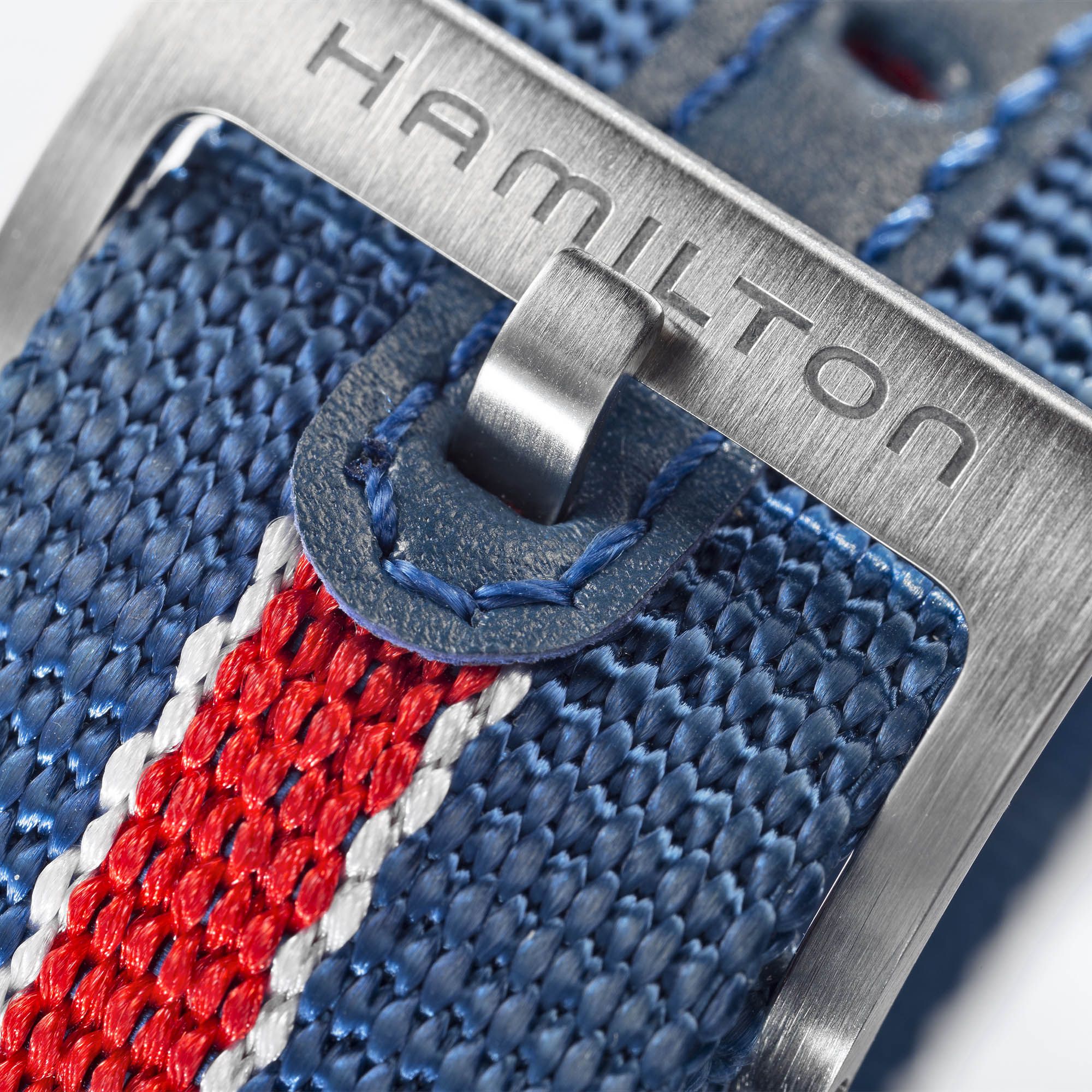Close-up of an engraved stainless steel pin buckle on a Hamilton red, white, and blue striped textile watch strap