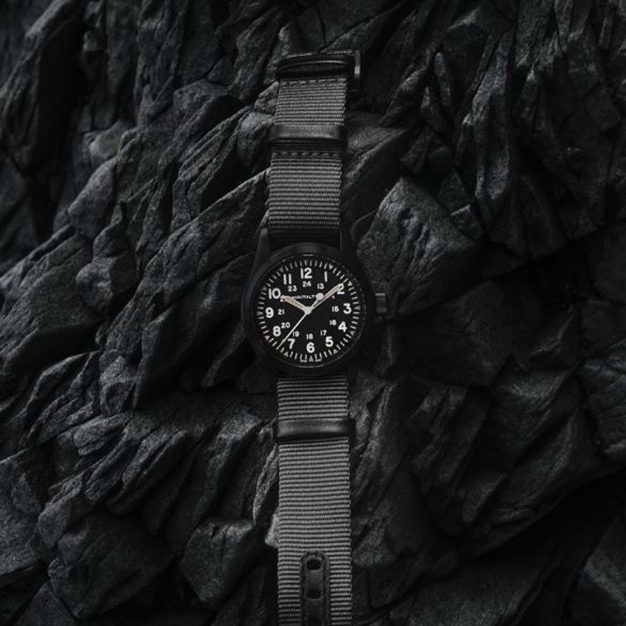 Hamilton Khaki Field black dial military watch with grey NATO strap viewed from above on rocky surface