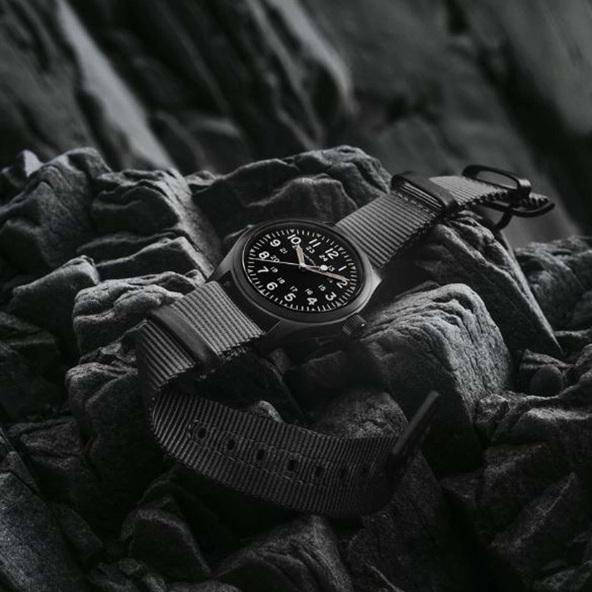Hamilton Khaki Field Automatic watch with black dial and grey NATO strap resting on dark rocks