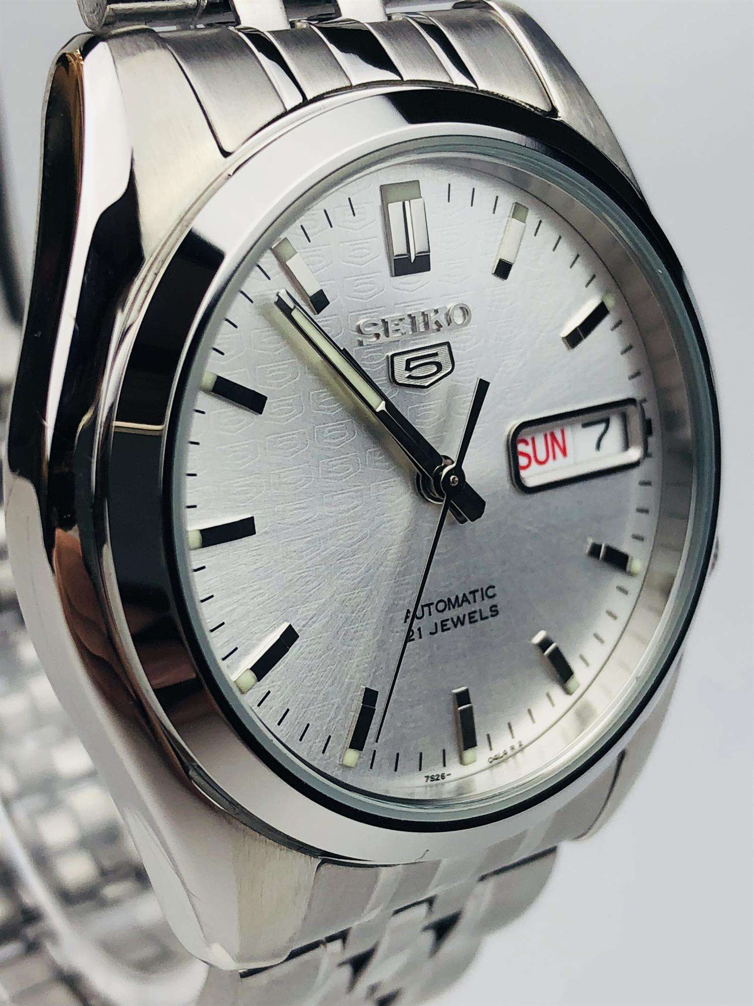 Detailed close-up of Seiko SNK355K1 silver textured dial showing Seiko 5 logo, luminous hands and day-date complication