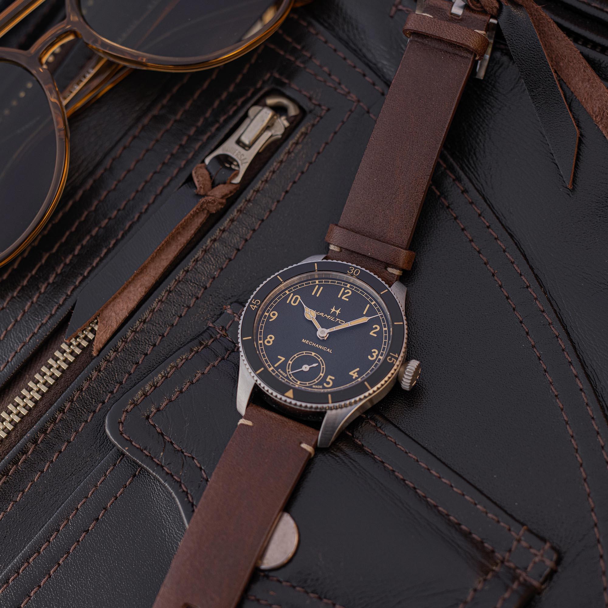 Hamilton Khaki Aviation Pilot Pioneer Mechanical watch with a black dial and brown leather strap, resting on a black leather jacket