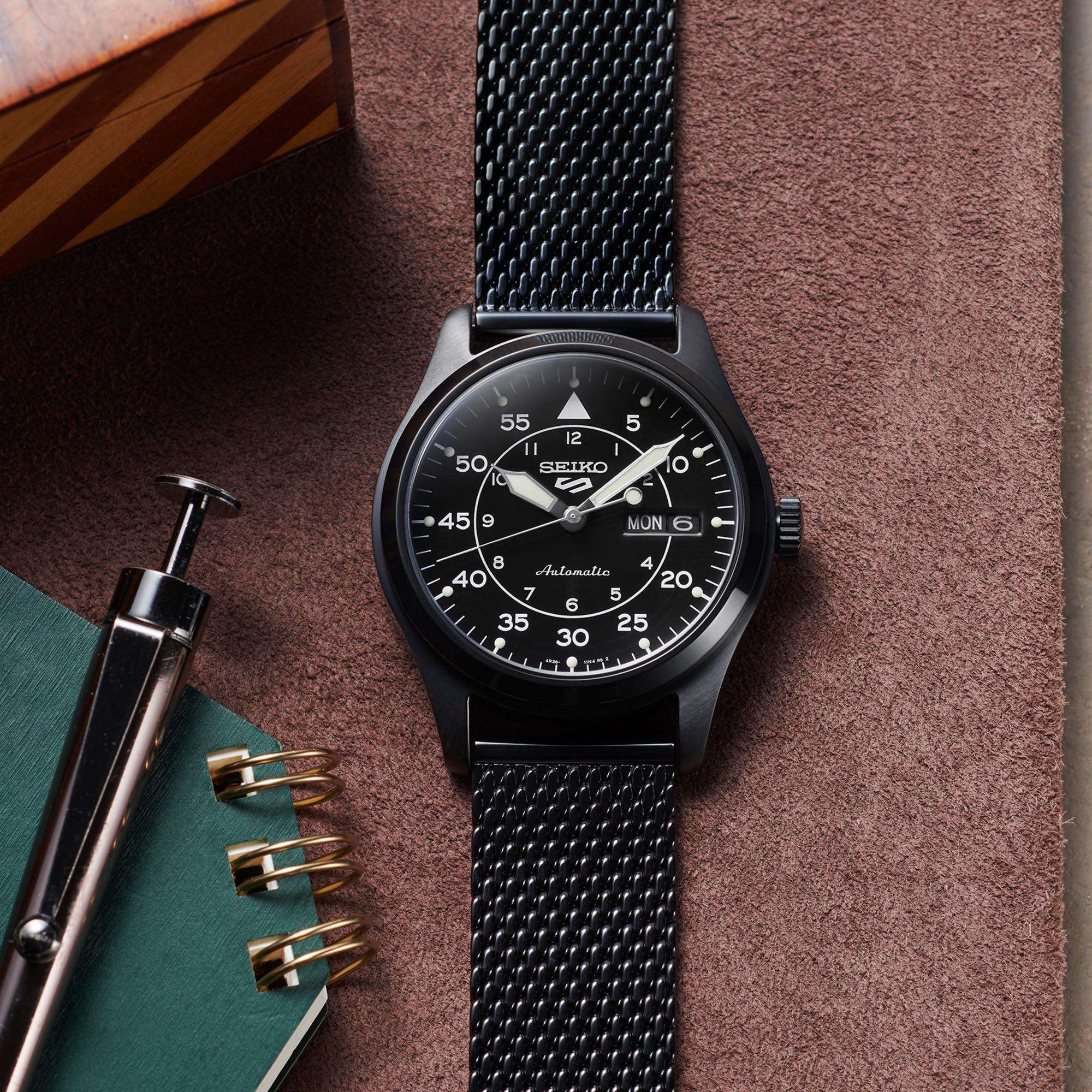 Black Seiko watch with mesh band on a textured surface