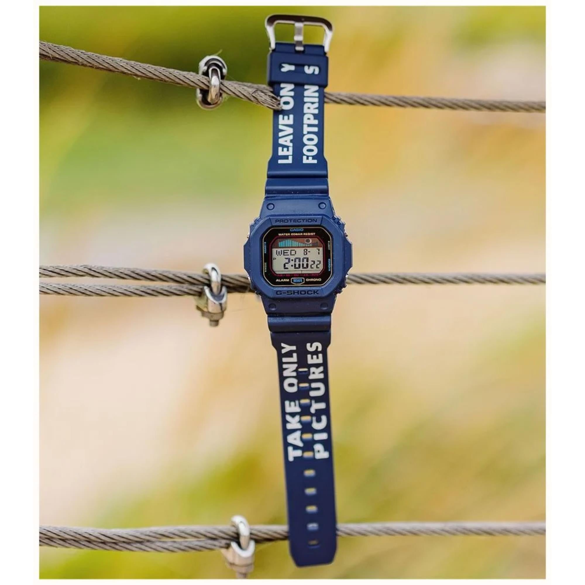Blue digital watch with motivational text on strap, hanging on a wire with a blurred natural background