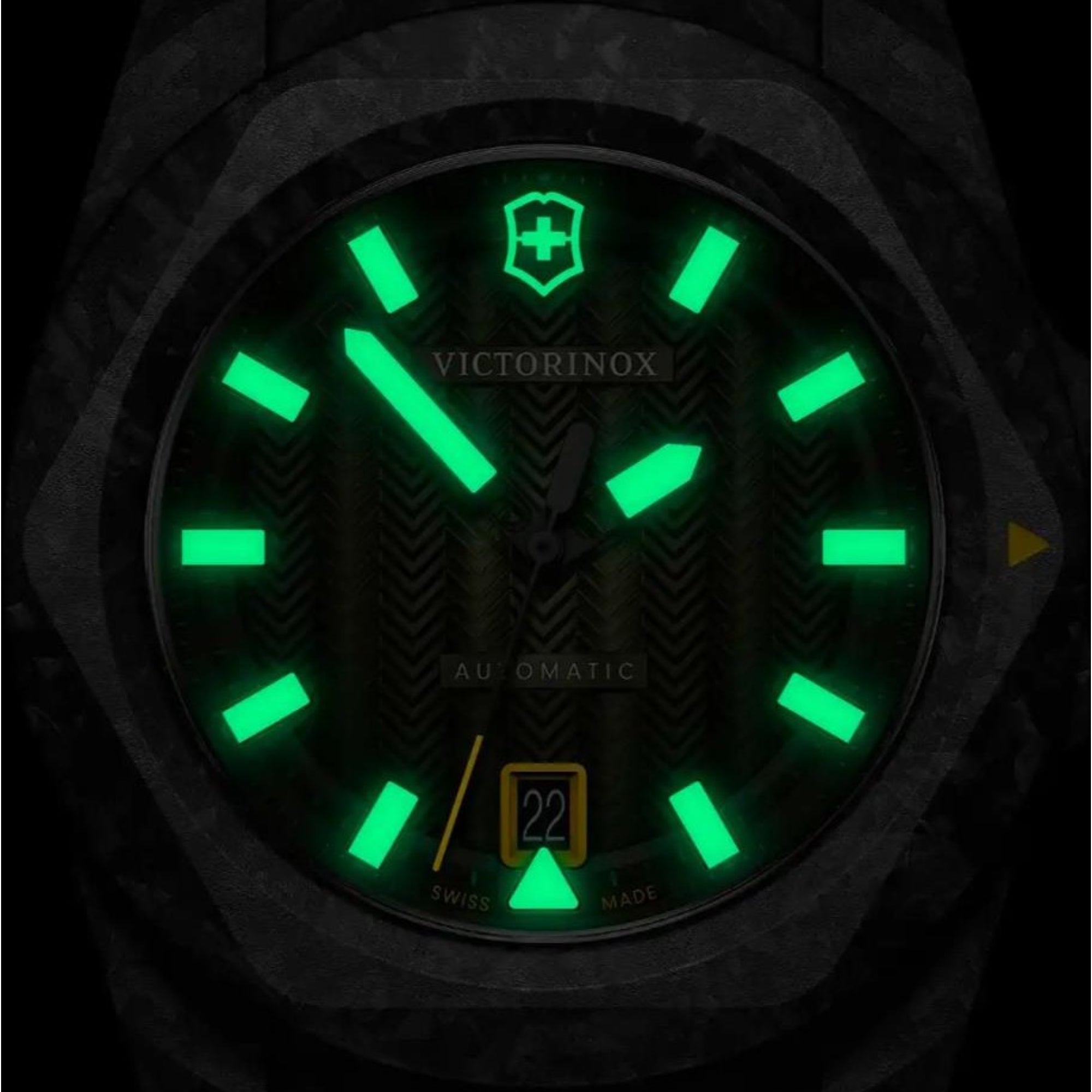Close-up of a Victorinox automatic watch in the dark, showcasing bright green luminous hour markers, hands, and logo.