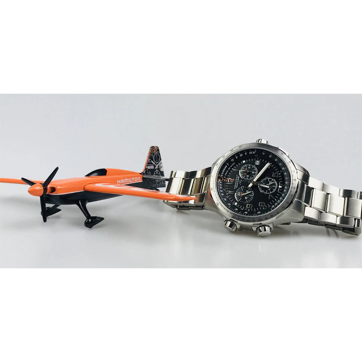 Hamilton chronograph watch with black dial and stainless steel bracelet displayed next to orange Hamilton airplane model