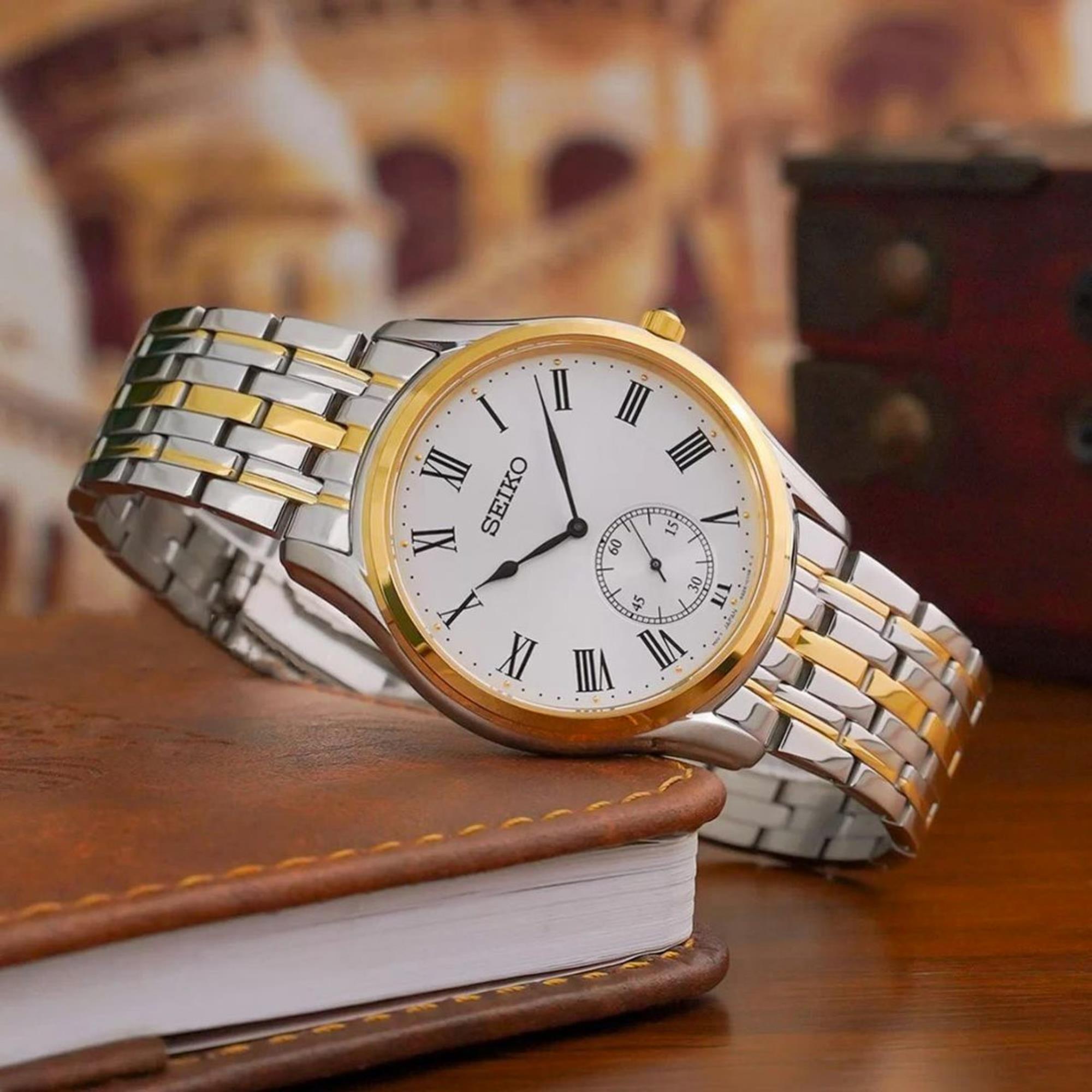 Seiko Essentials watch SKU SRK048P1 with a white dial and two-tone bracelet, resting across a brown leather notebook