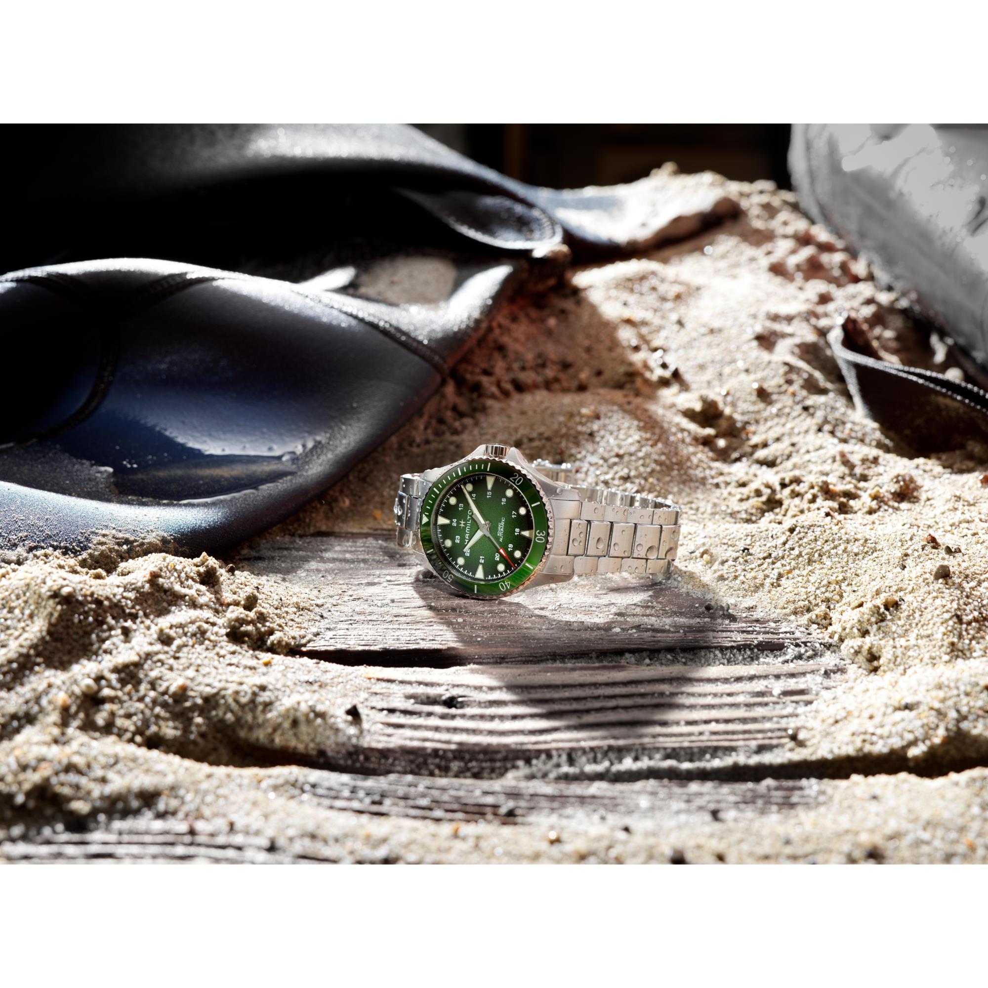 Hamilton Khaki Navy Scuba Automatic green dial dive watch with stainless steel bracelet resting on sand with diving equipment