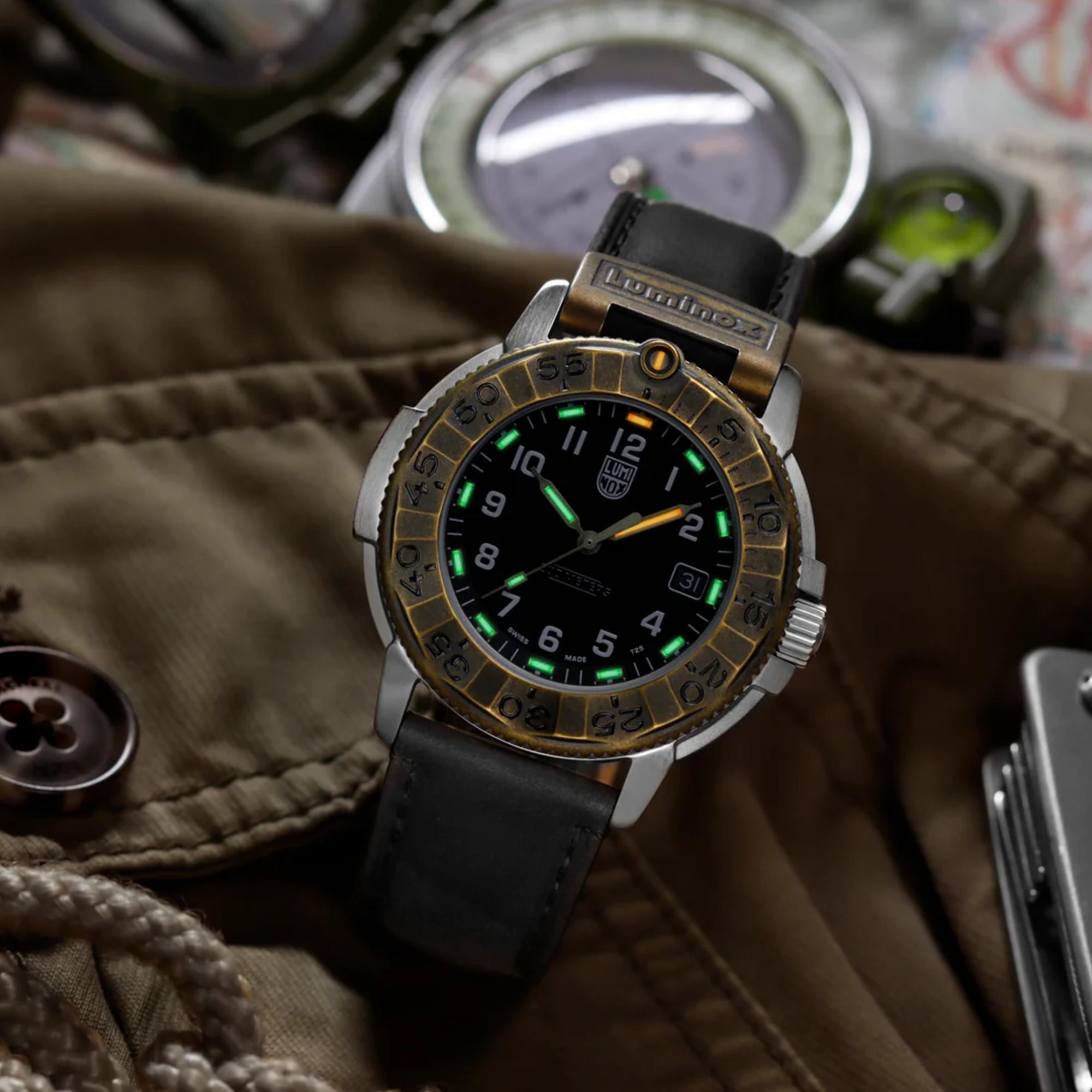 Luminox Adventure Watch XL.1301 resting on a brown utility jacket next to outdoor gear, showing its glowing hands, black leather strap, and textured bronze bezel