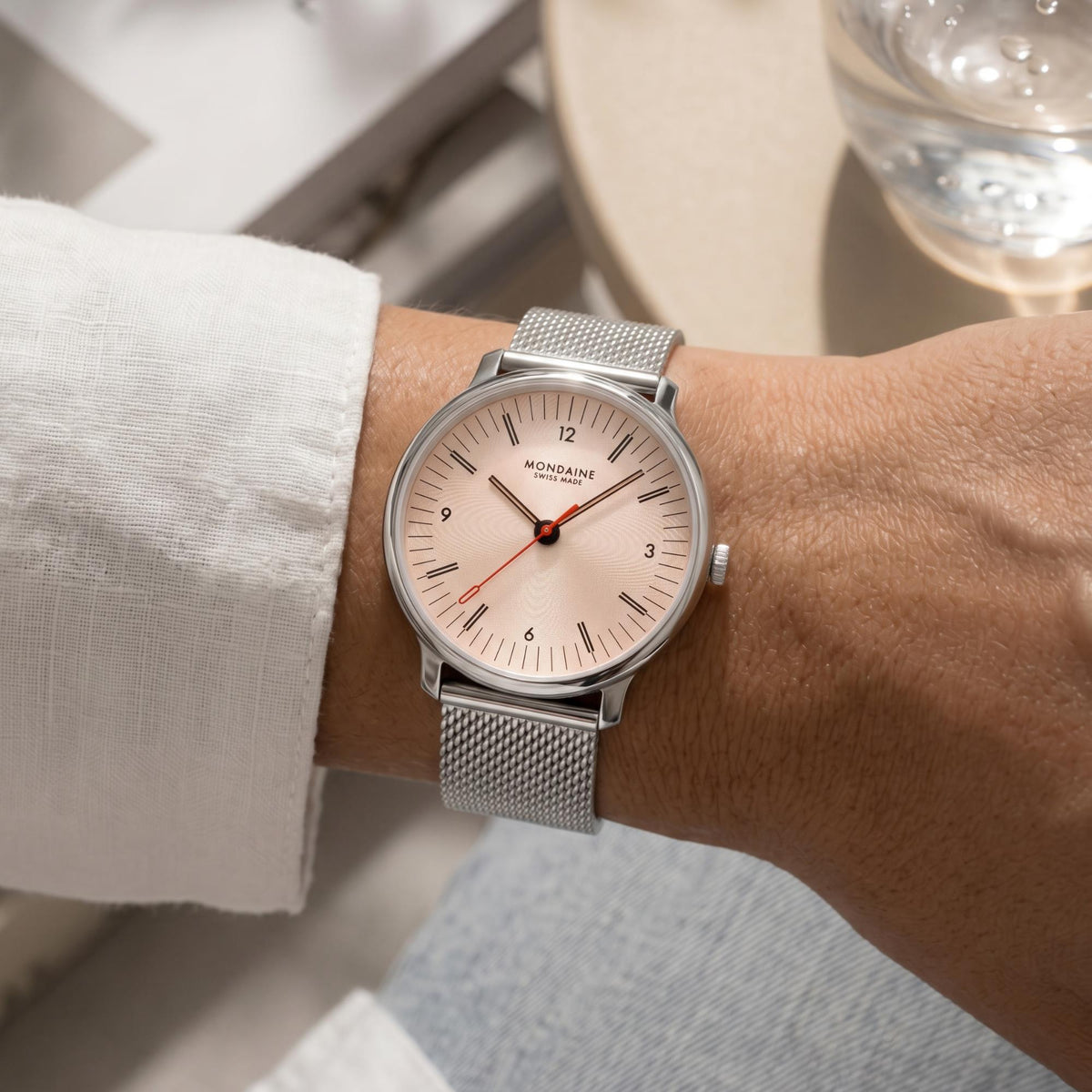 A wrist shot view of the Mondaine Doppio ladies quartz watch MLE.33150.SM paired with a white shirt sleeve, demonstrating its clean aesthetic and readable dial in soft, warm indoor lighting