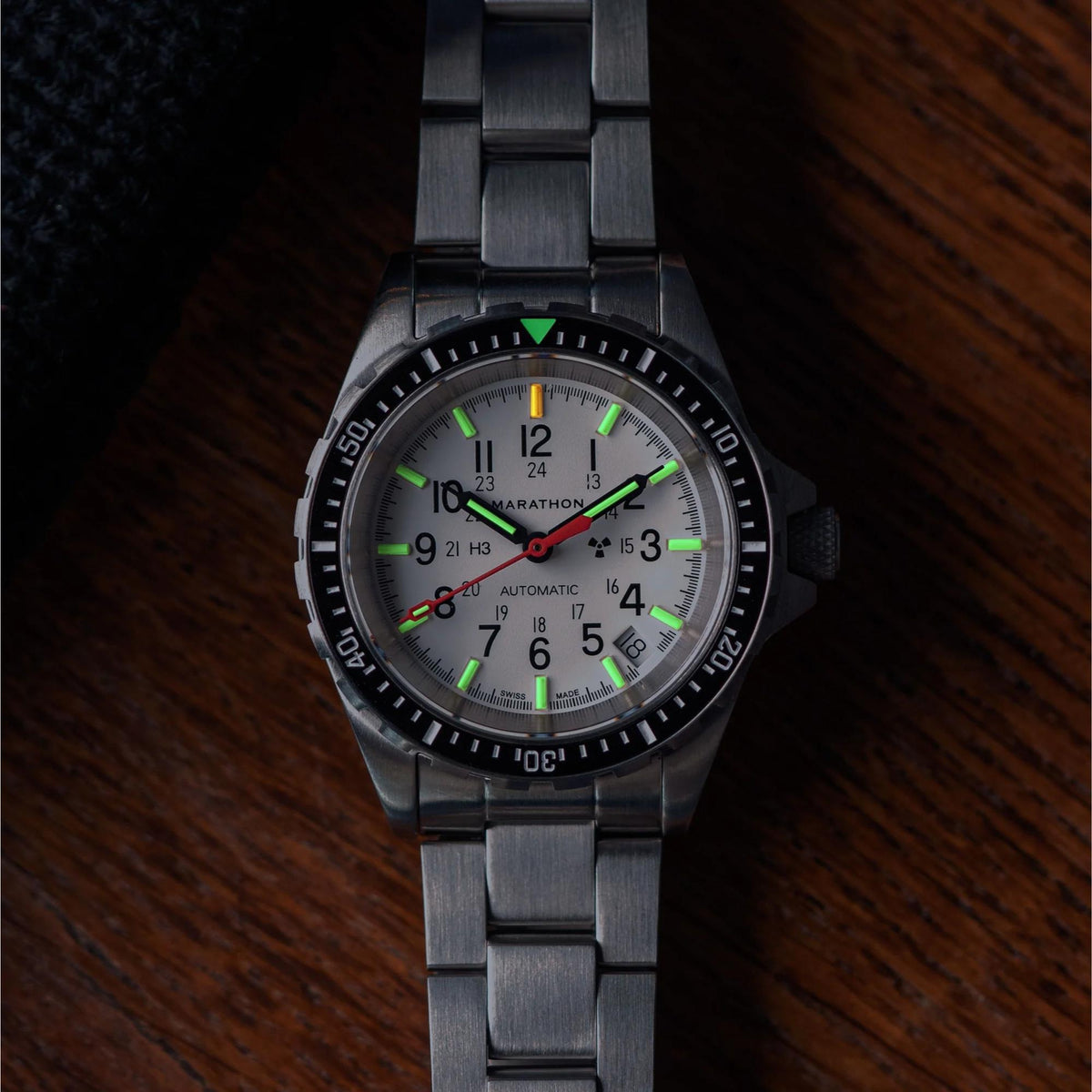 Marathon MSAR Arctic Edition WW194026SS-0506 watch displayed on a wooden surface showing illuminated tritium markers