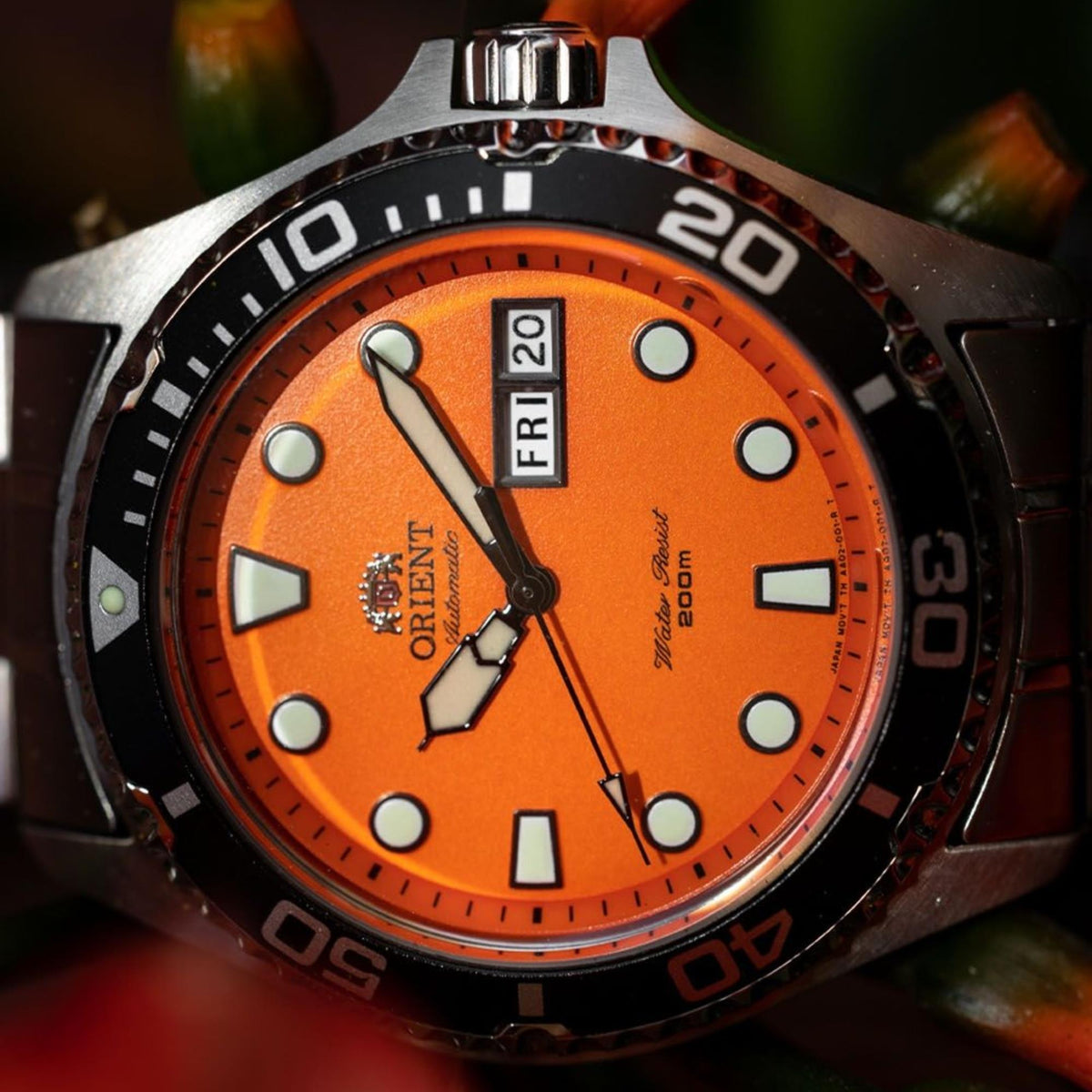 Orient Ray TAA02006M9 close-up view of orange dial face with luminous hour markers, hands, and day-date display