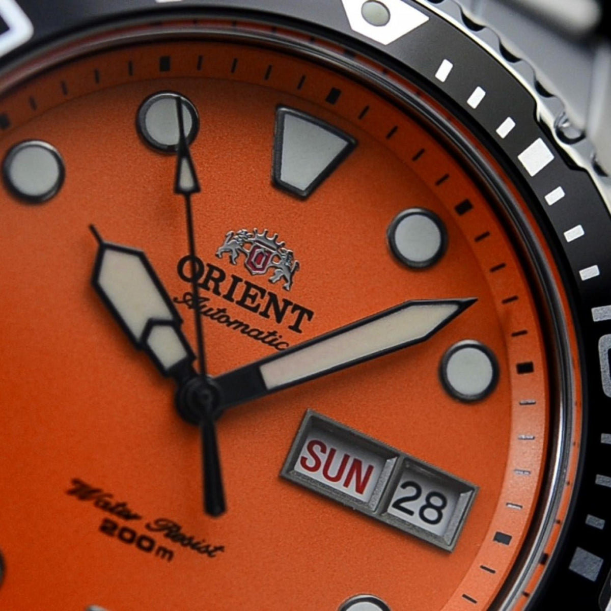 Orient Ray TAA02006M9 macro shot highlighting orange dial, hands, logo, and rotating bezel detail
