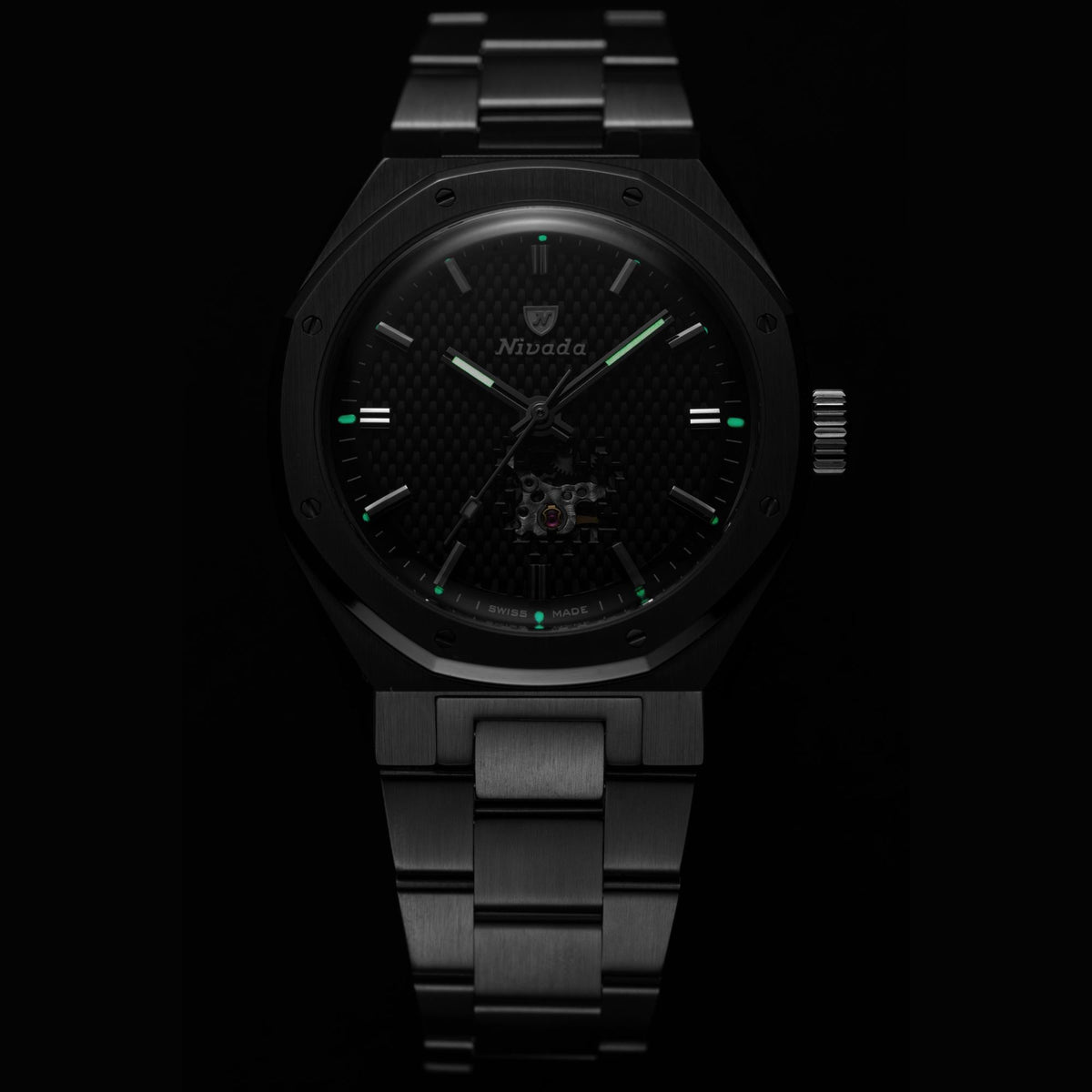 Nivada Grenchen F77 MK2 68023A77 luminous hands and hour markers glowing green against dark embossed carbon dial in dim lighting