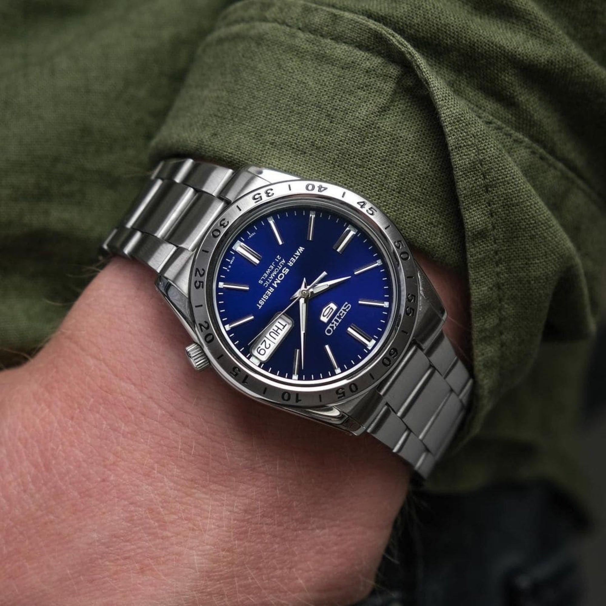 Seiko SNKD99K1 automatic watch worn on wrist with green jacket sleeve in lifestyle setting